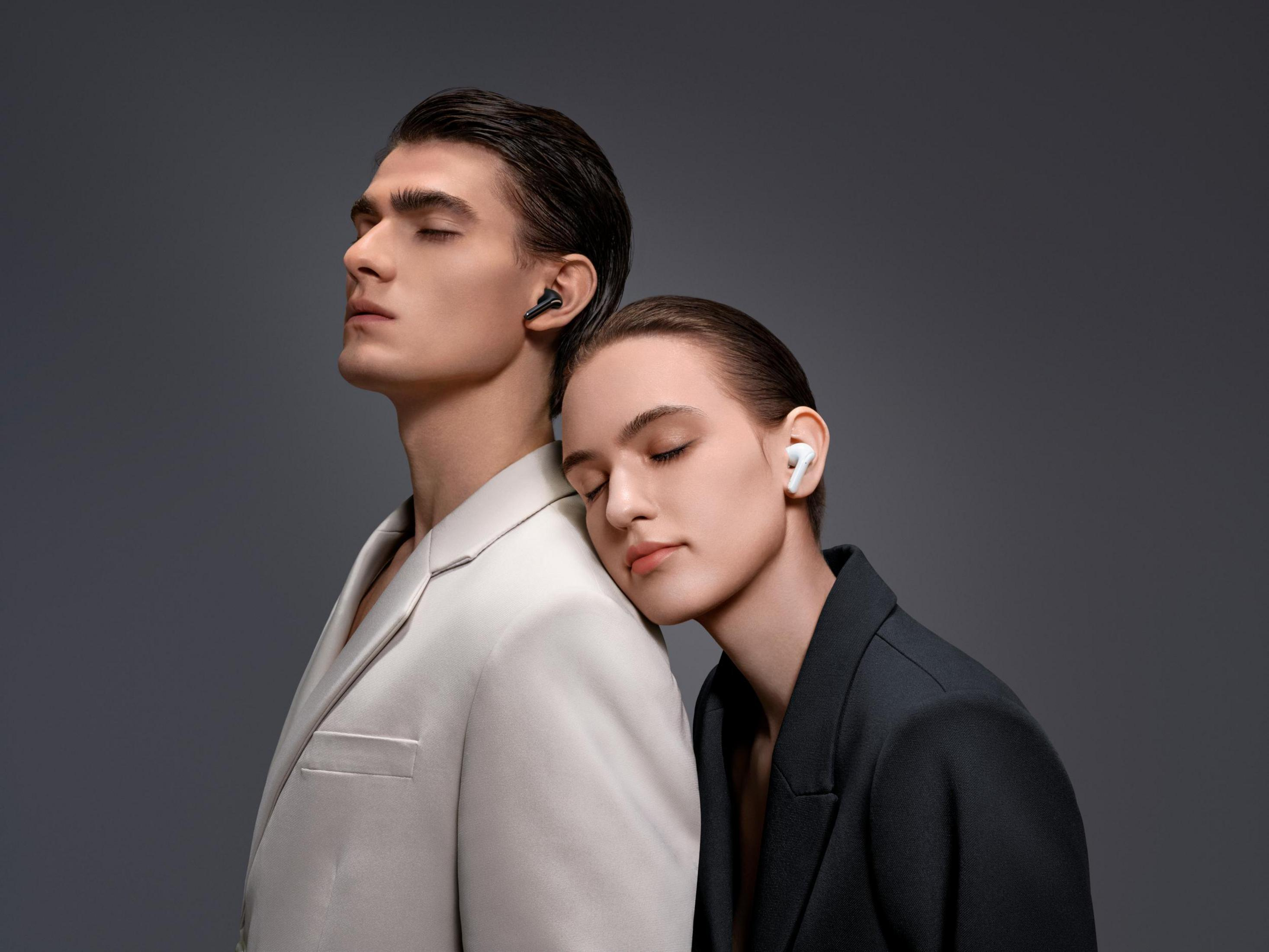 Mann und Frau mit Ohrhörern. Frau lehnt am Rücken des Mannes. Beide Augen zu.