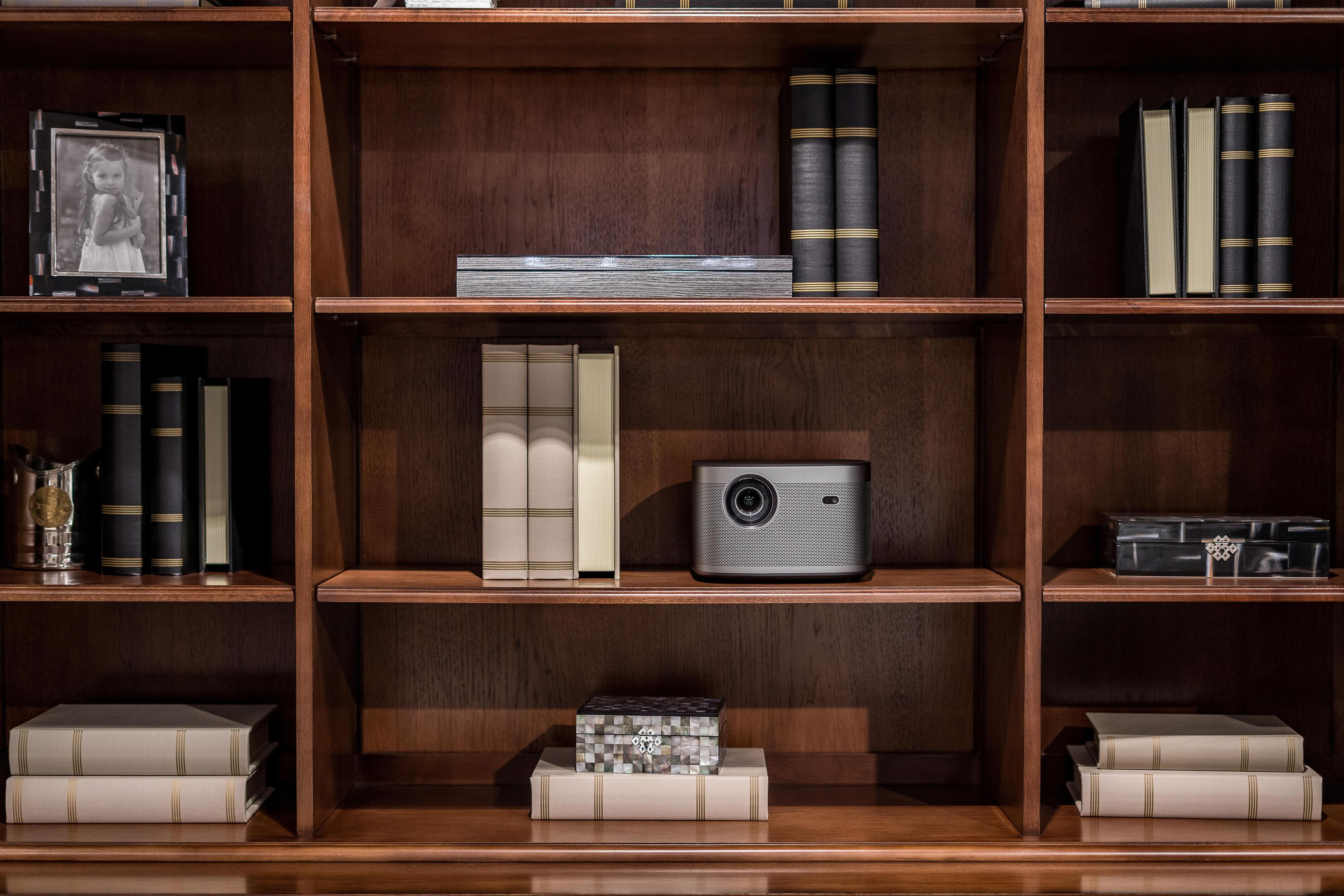 Libreria in legno con libri, un proiettore e oggetti decorativi.