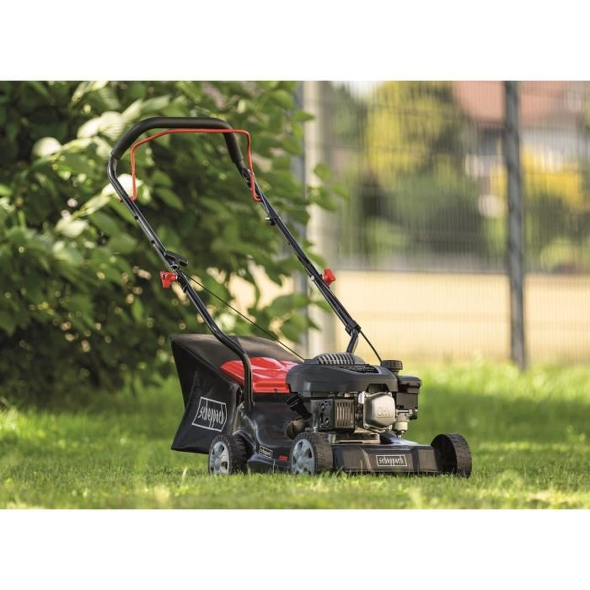 Een grasmaaier op groen gras met een rode en zwarte zak, in een achtertuin.