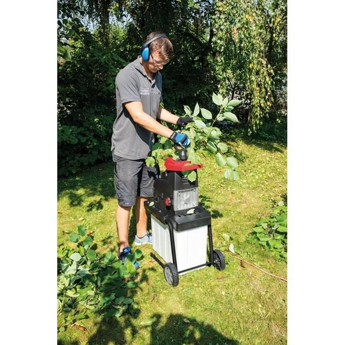 Een man die een hakselaar gebruikt in een tuin. Hij draagt een veiligheidsbril en gehoorbescherming.
