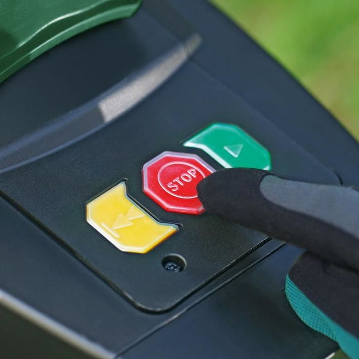 Gros plan d'une main appuyant sur un bouton d'arrêt rouge sur une machine noire avec des boutons verts et jaunes.
