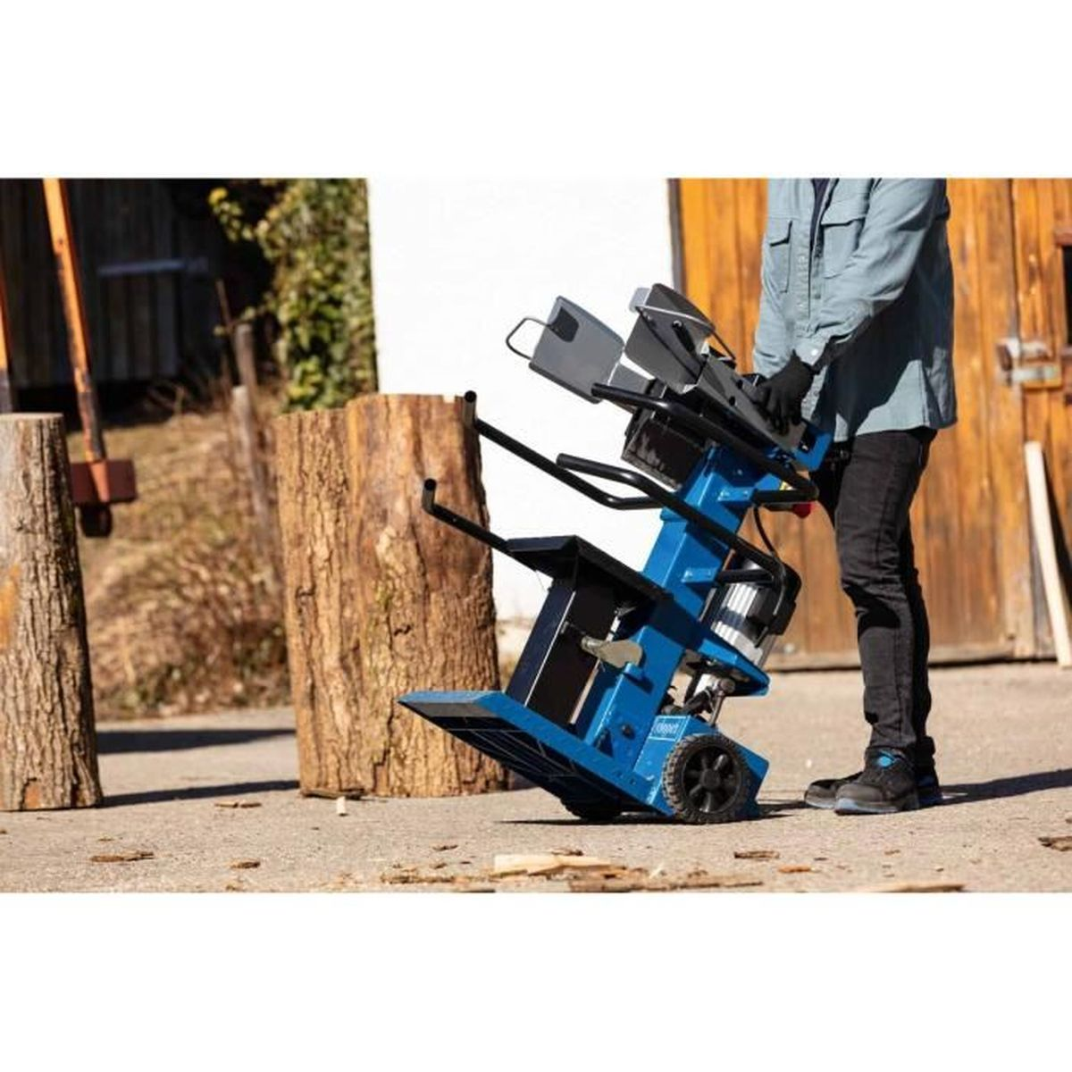 Ein Mann bedient einen Holzspalter. Der Spalter ist blau und steht auf Beton.
