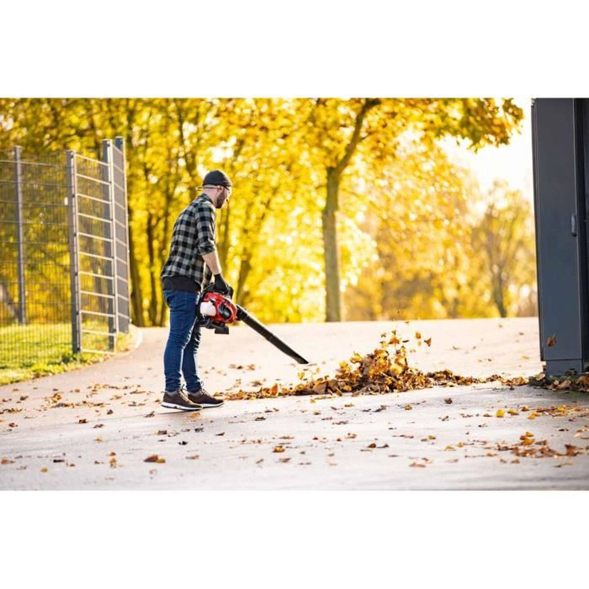 Mężczyzna używa dmuchawy do liści, scena jesienna.