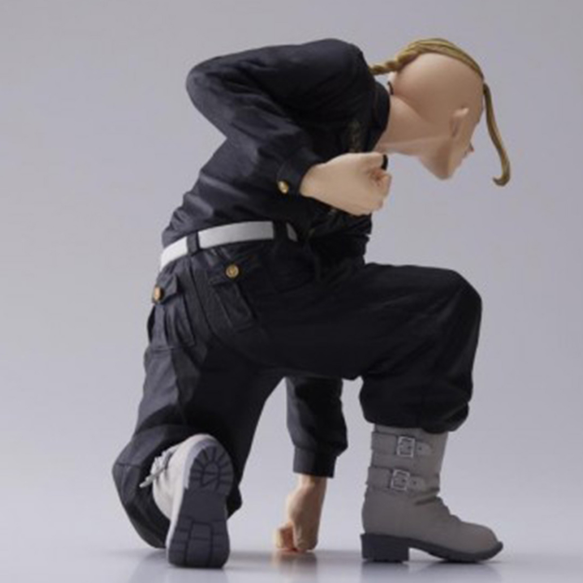 Figura de anime de un hombre arrodillado con ropa negra, botas blancas y trenza rubia, sobre superficie gris.