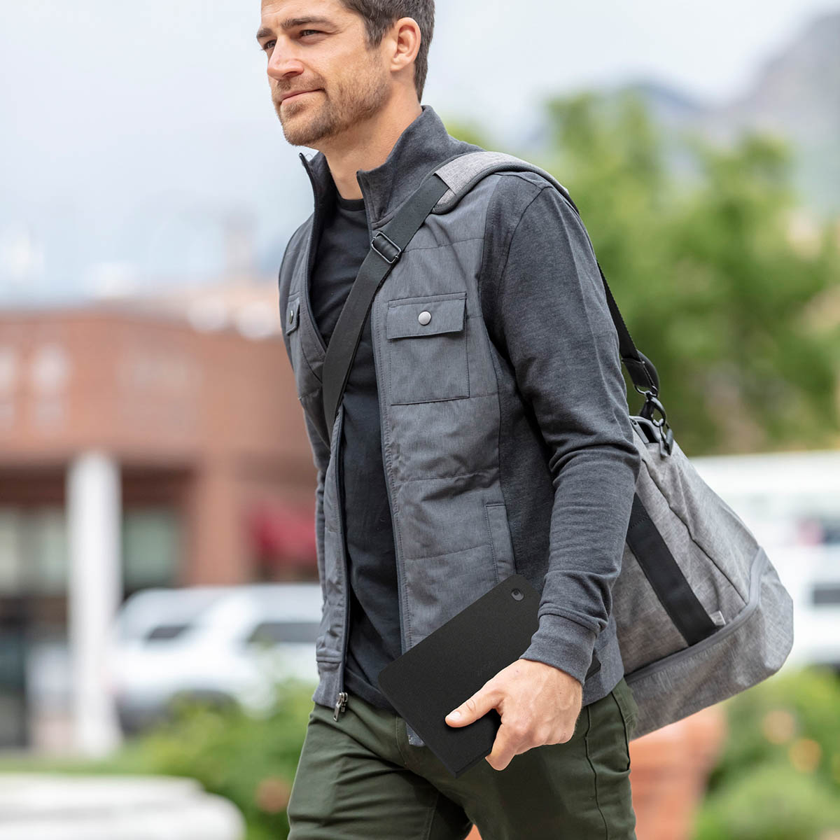 Man die een tablet in een zwarte hoes en een tas draagt. Hij loopt buiten.