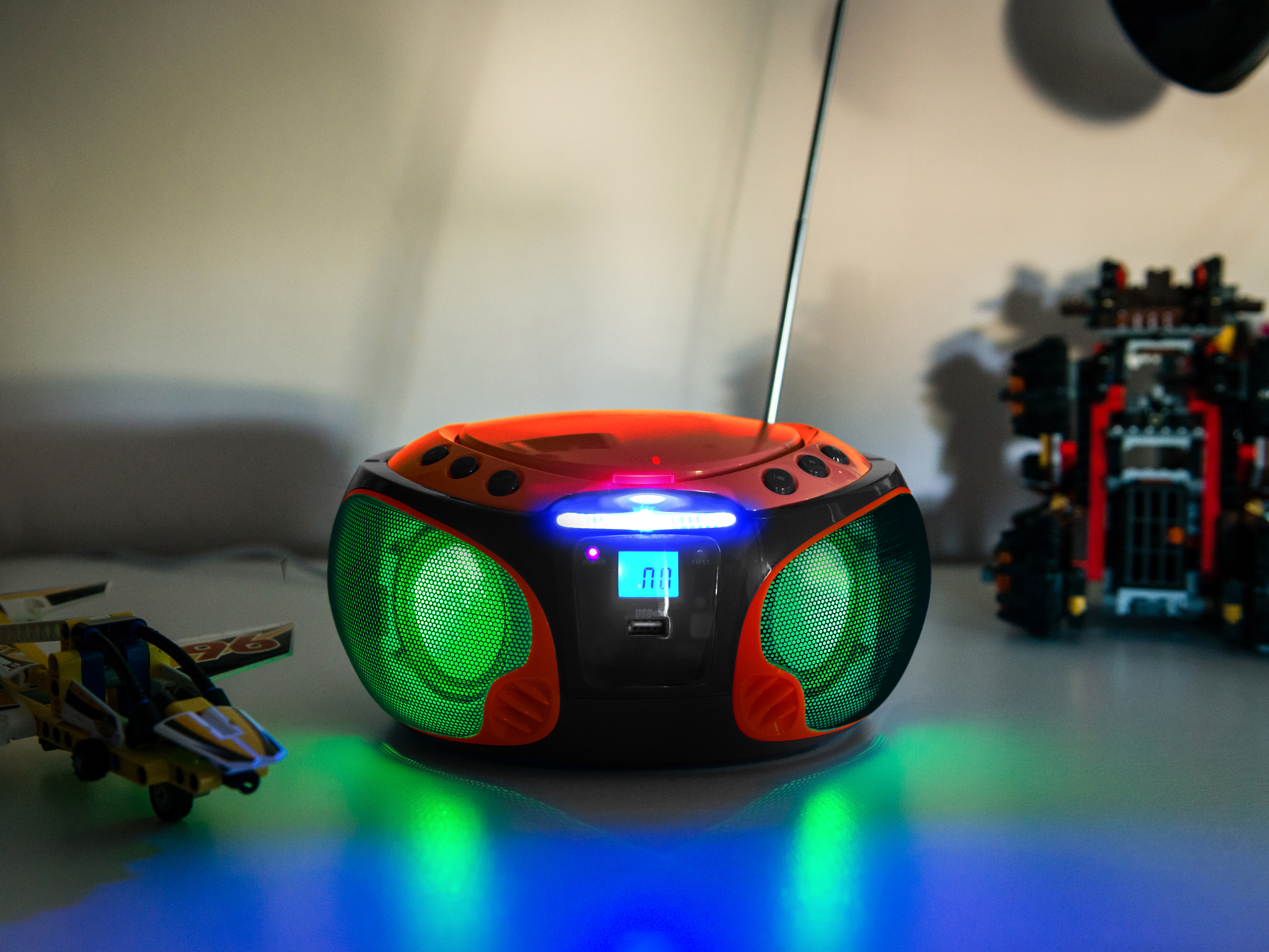 Boombox with green speakers, orange top, and a digital display. Toys are on either side.