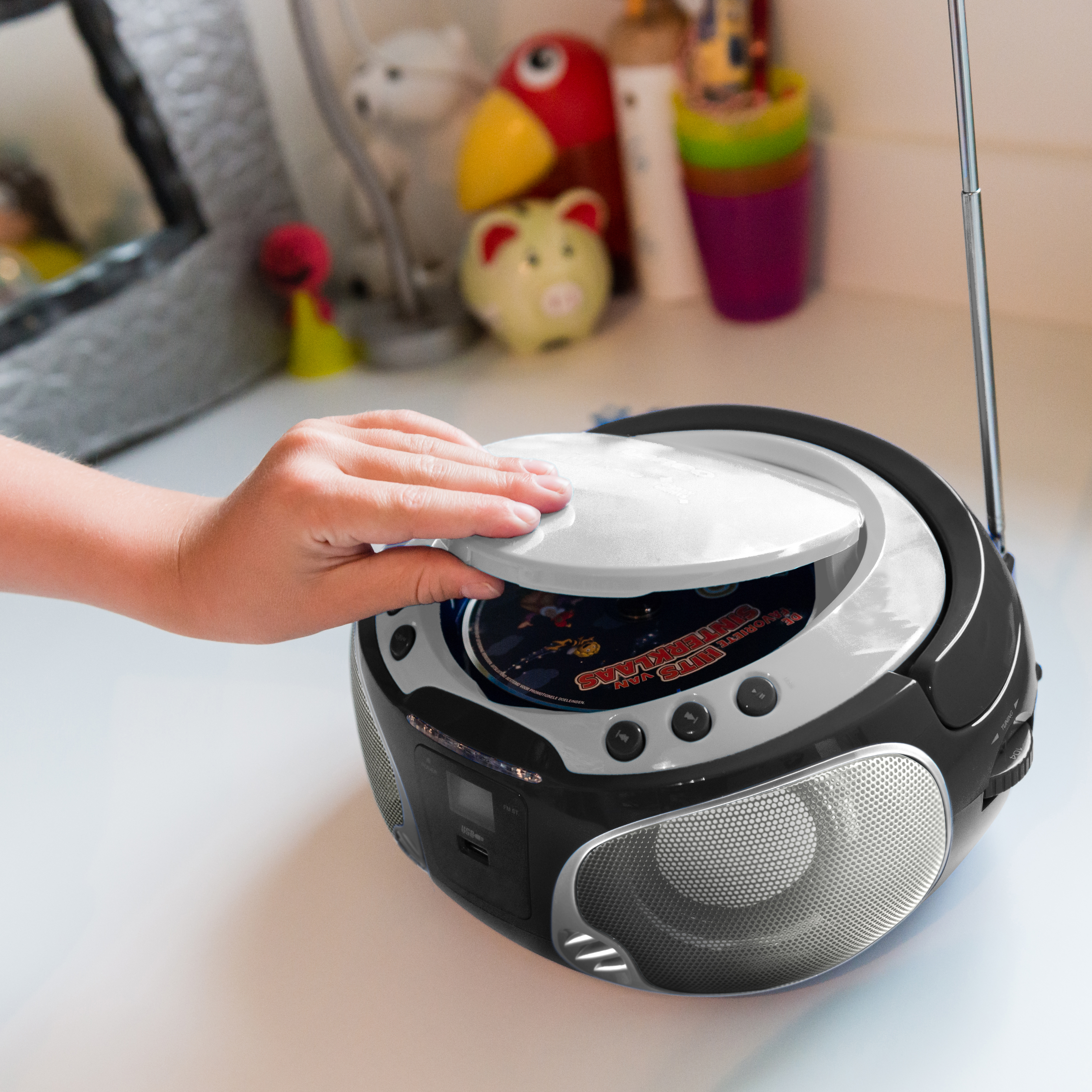 A person's hand opening a black and silver CD player on a white surface.