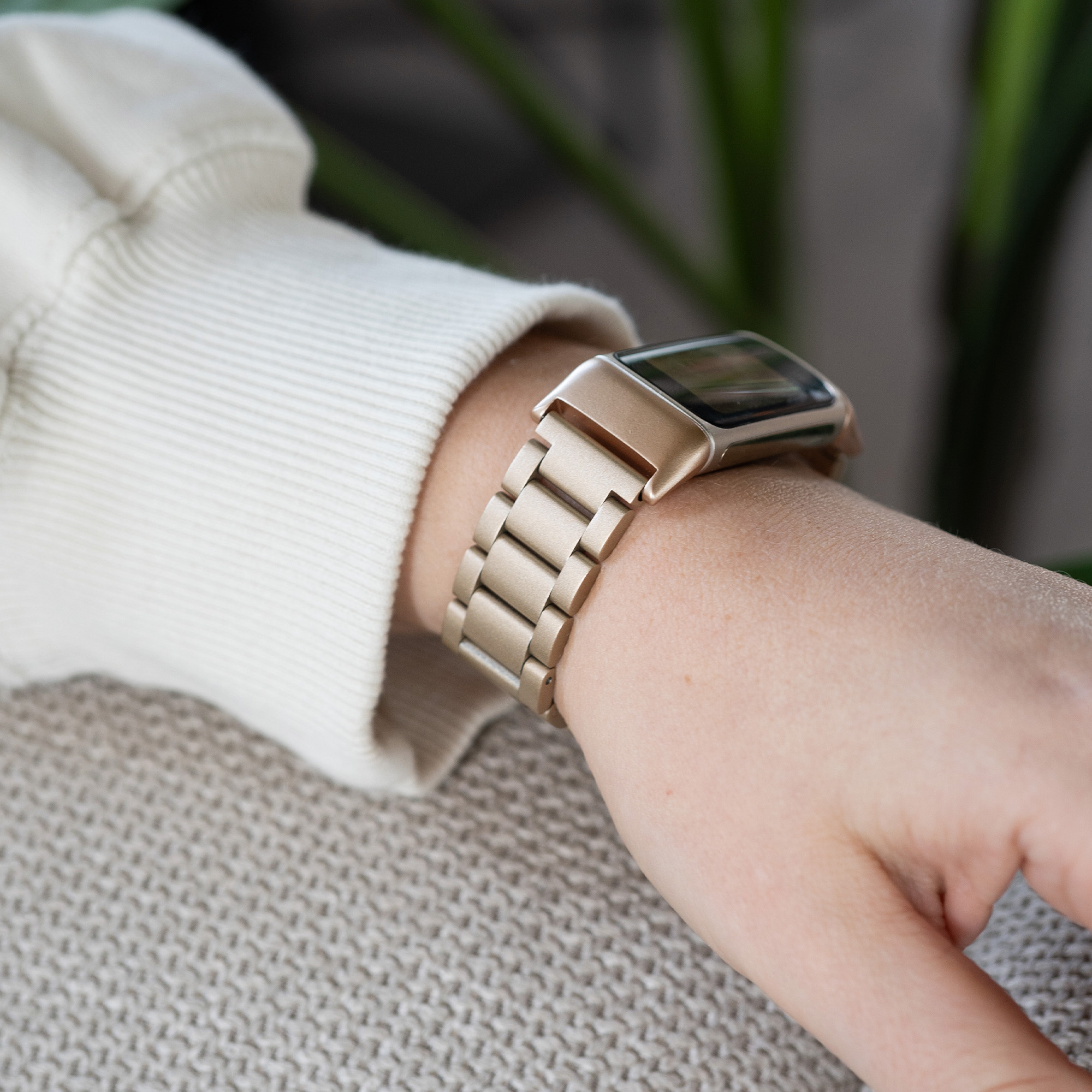 Ein Handgelenk mit einer goldenen Uhr mit goldenem Metallarmband. Die Uhr befindet sich auf einer beigen Strickoberfläche.