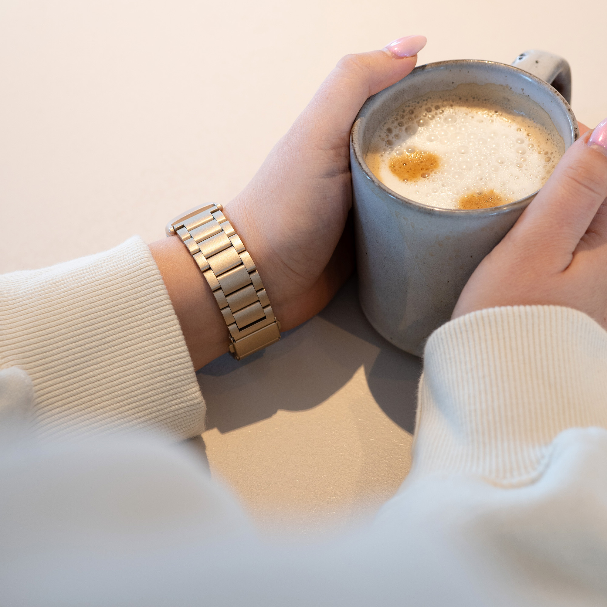 Hände halten eine Tasse Kaffee mit Schaum. Das Handgelenk hat eine goldene Metalluhr.