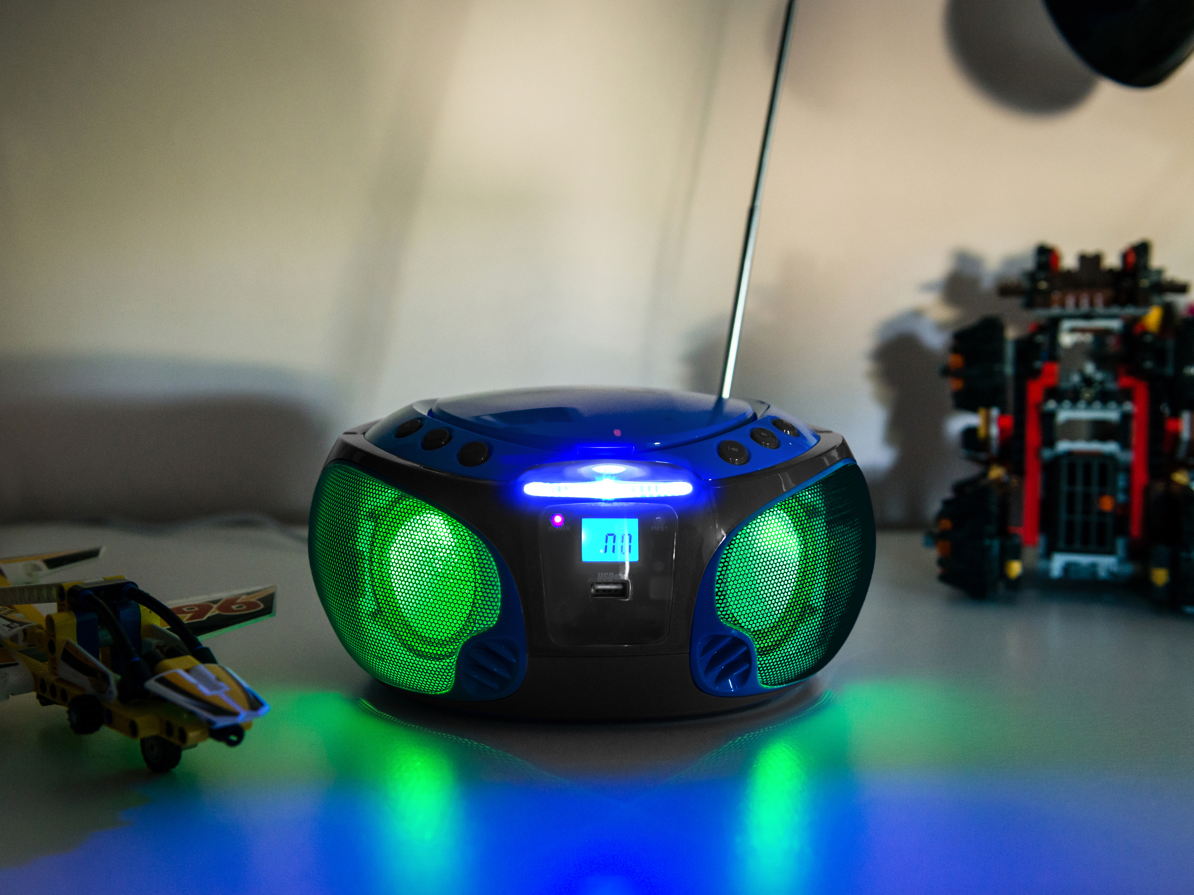 A blue and black radio with green lights, with toy cars on the table.