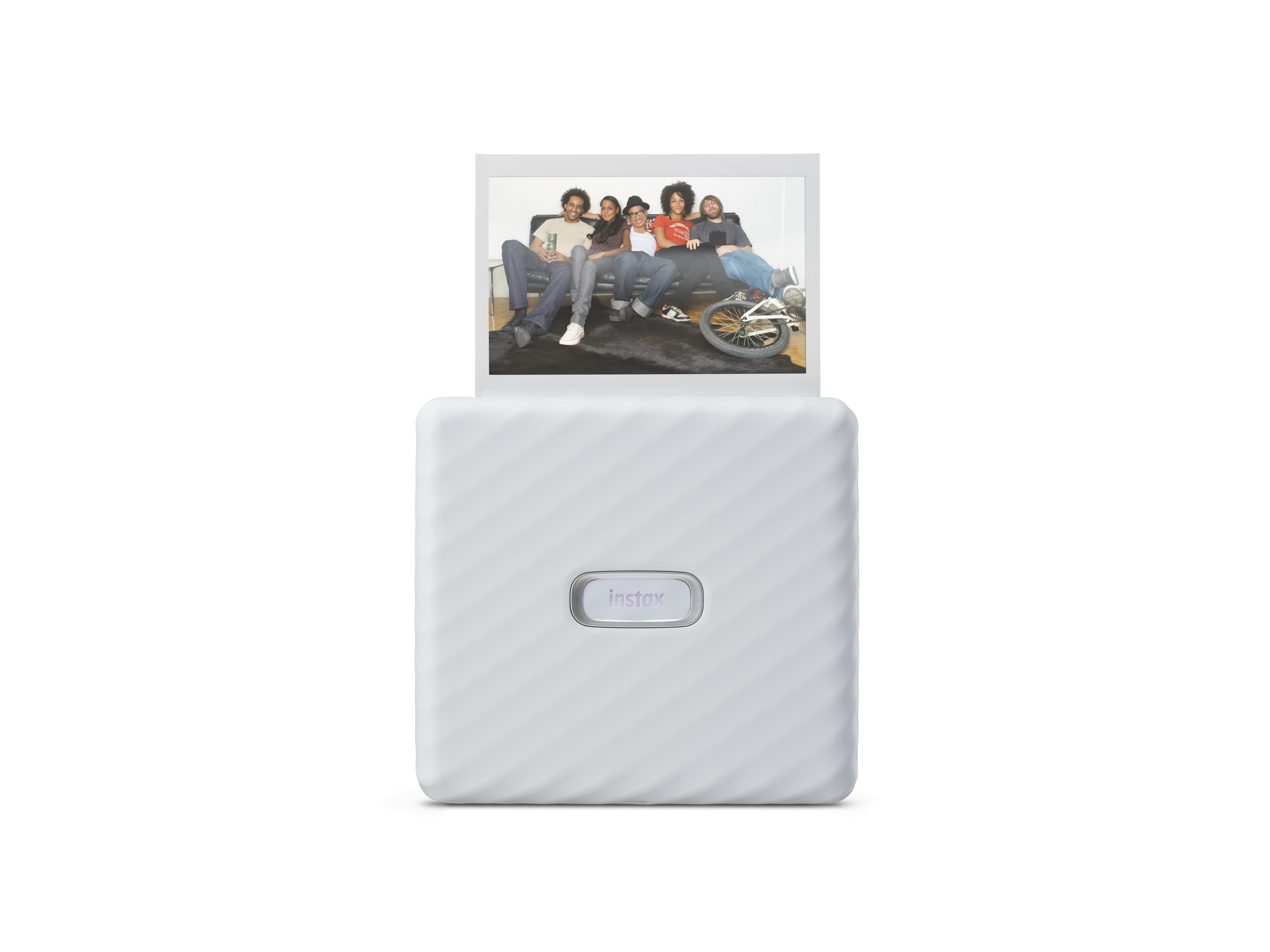 Una stampante Instax bianca stampa una foto di cinque persone su un divano. La stampante è su sfondo bianco.