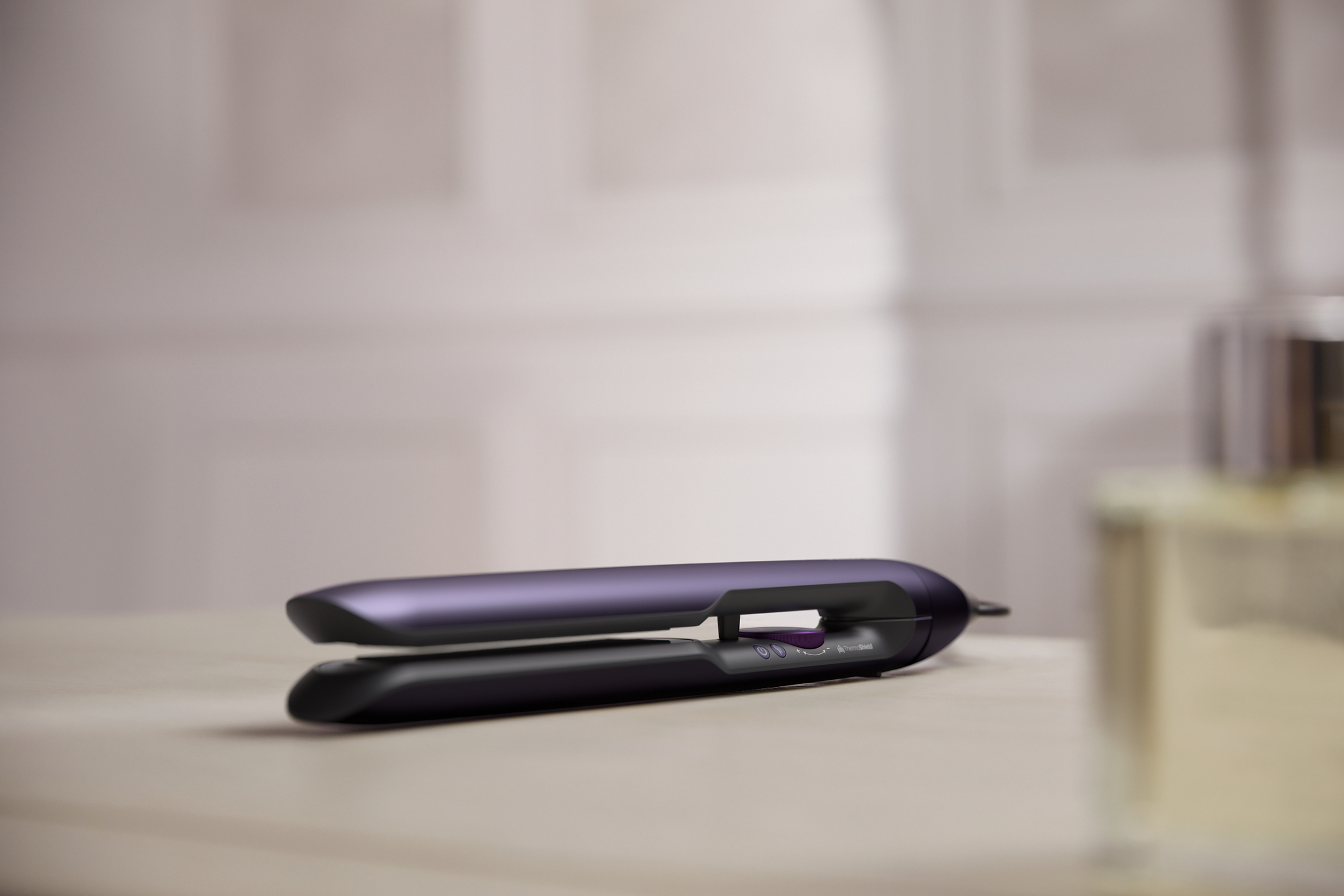 Fioletowa prostownica do włosów, na stole, z rozmytą butelką perfum, beżowe otoczenie.