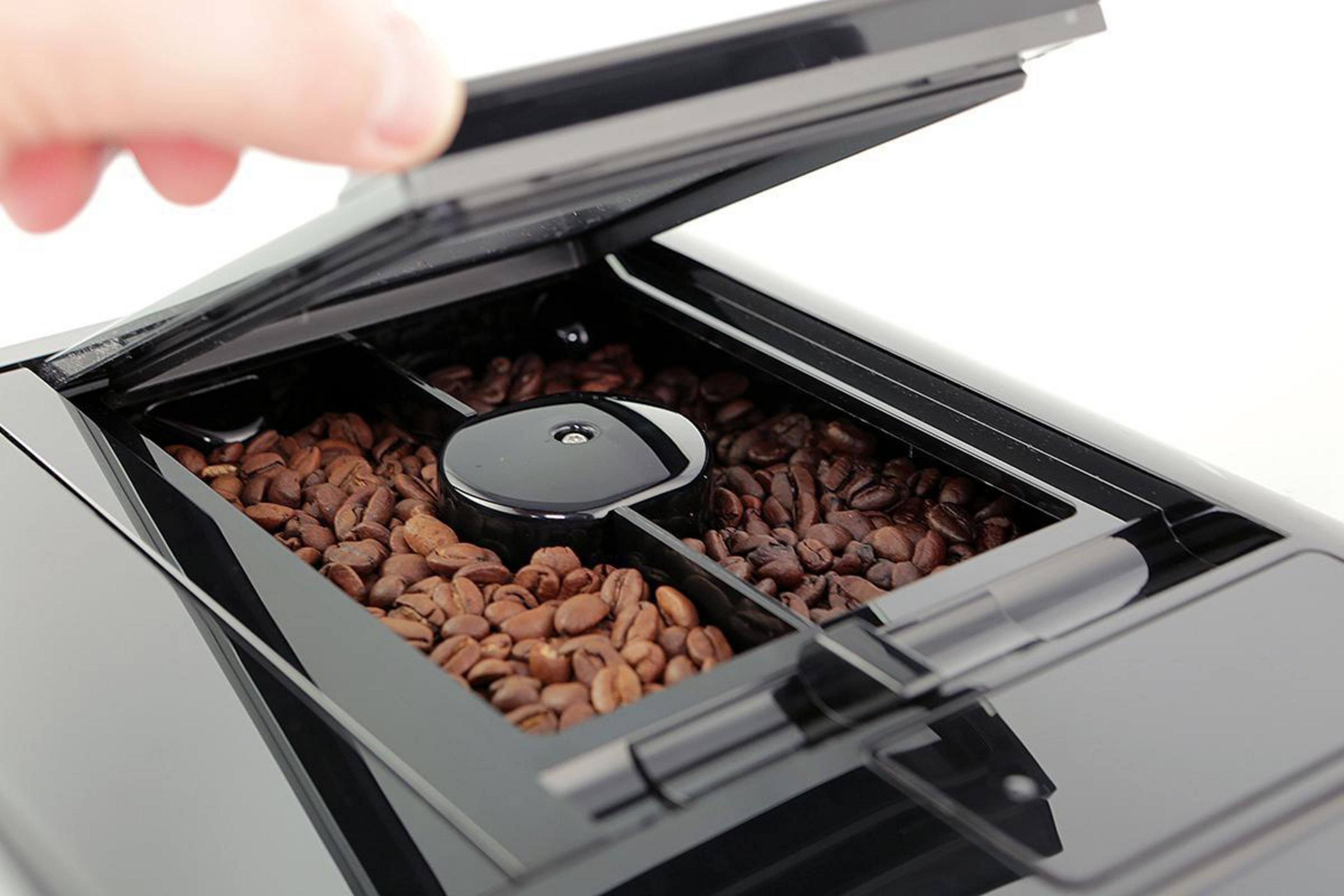 Kaffeebohnen in einem Kaffeemaschinenfach. Eine Hand öffnet den Deckel.