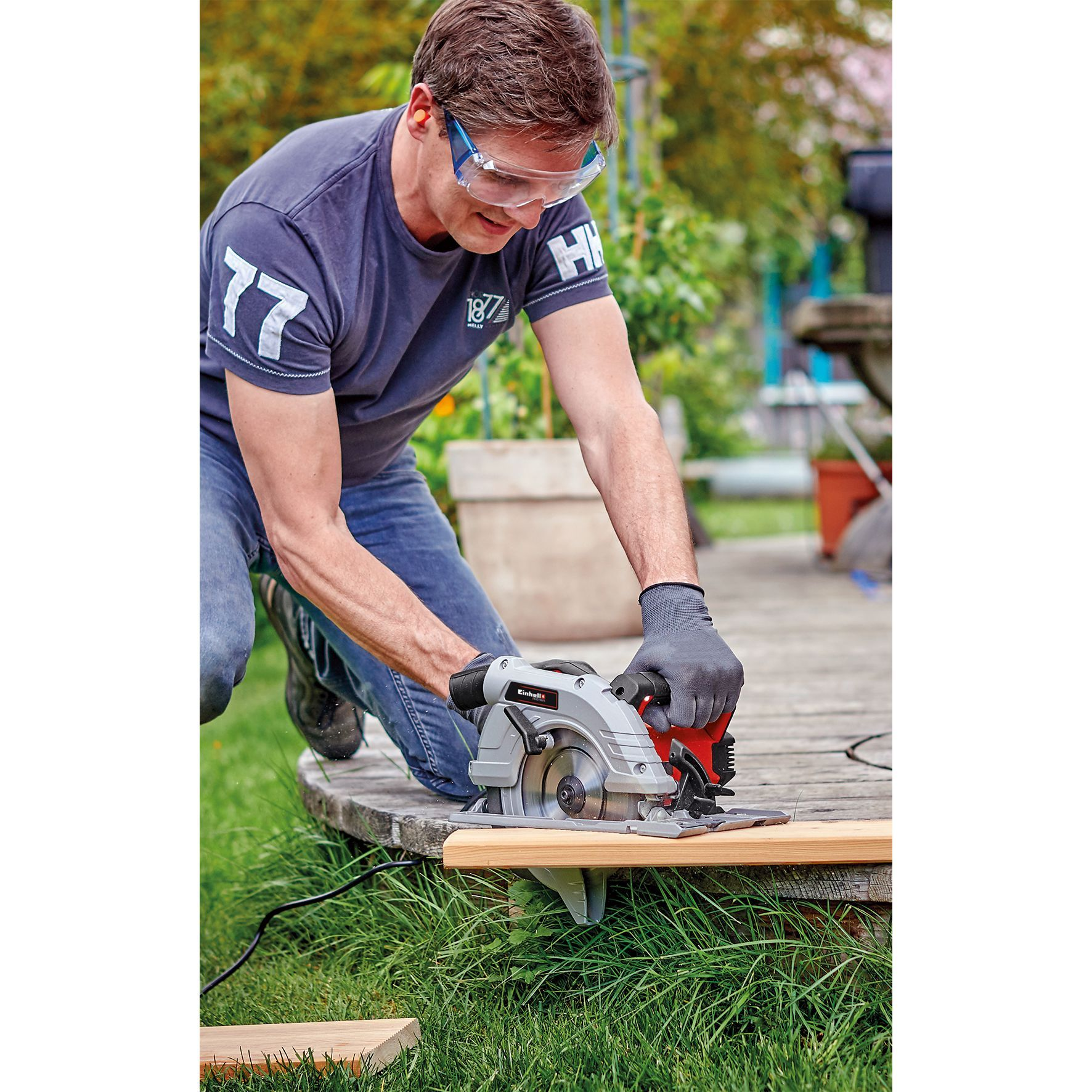 Mężczyzna używa piły tarczowej na drewnianej desce na zewnątrz.