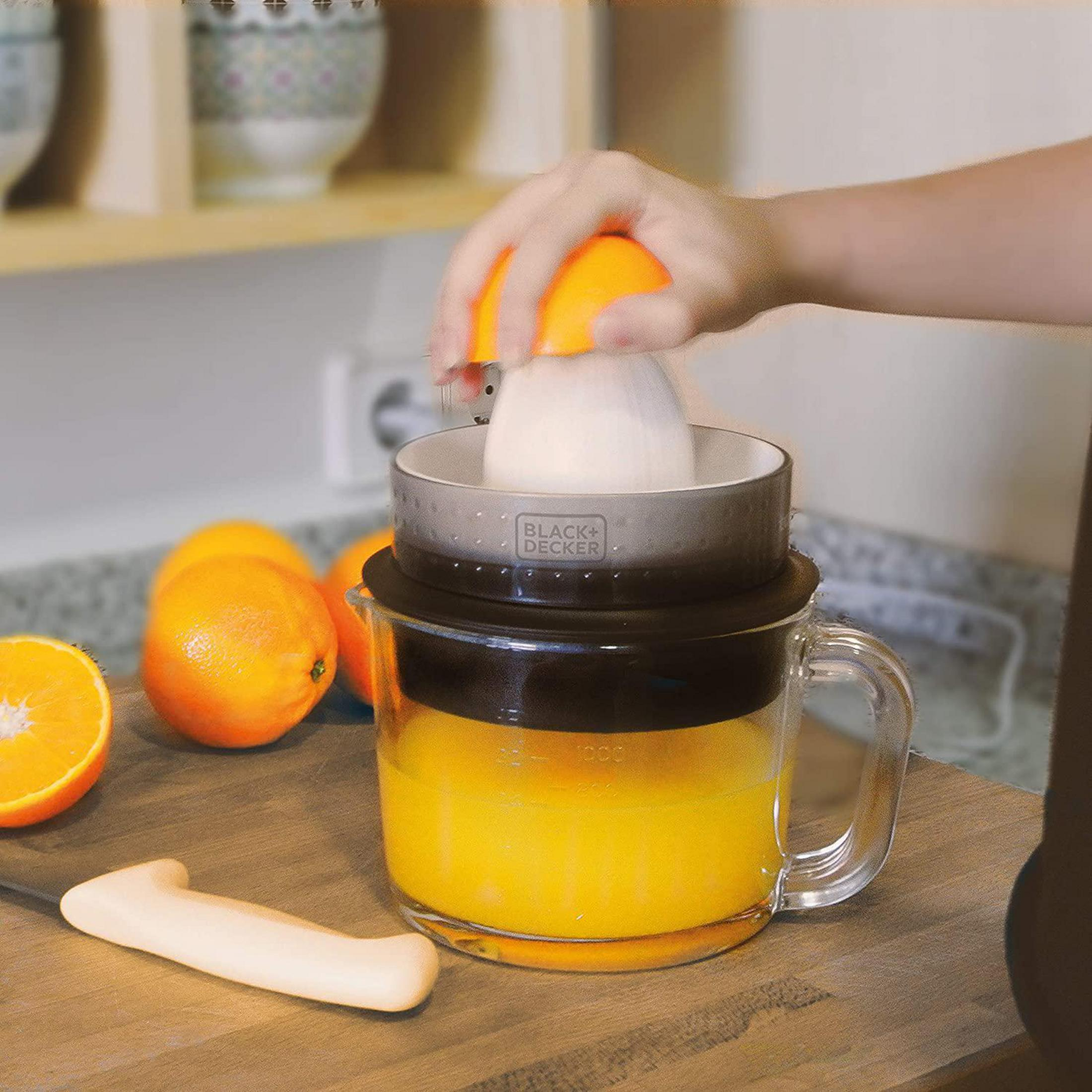 Persona exprimiendo una naranja con un exprimidor. Se ve zumo de naranja en el vaso.