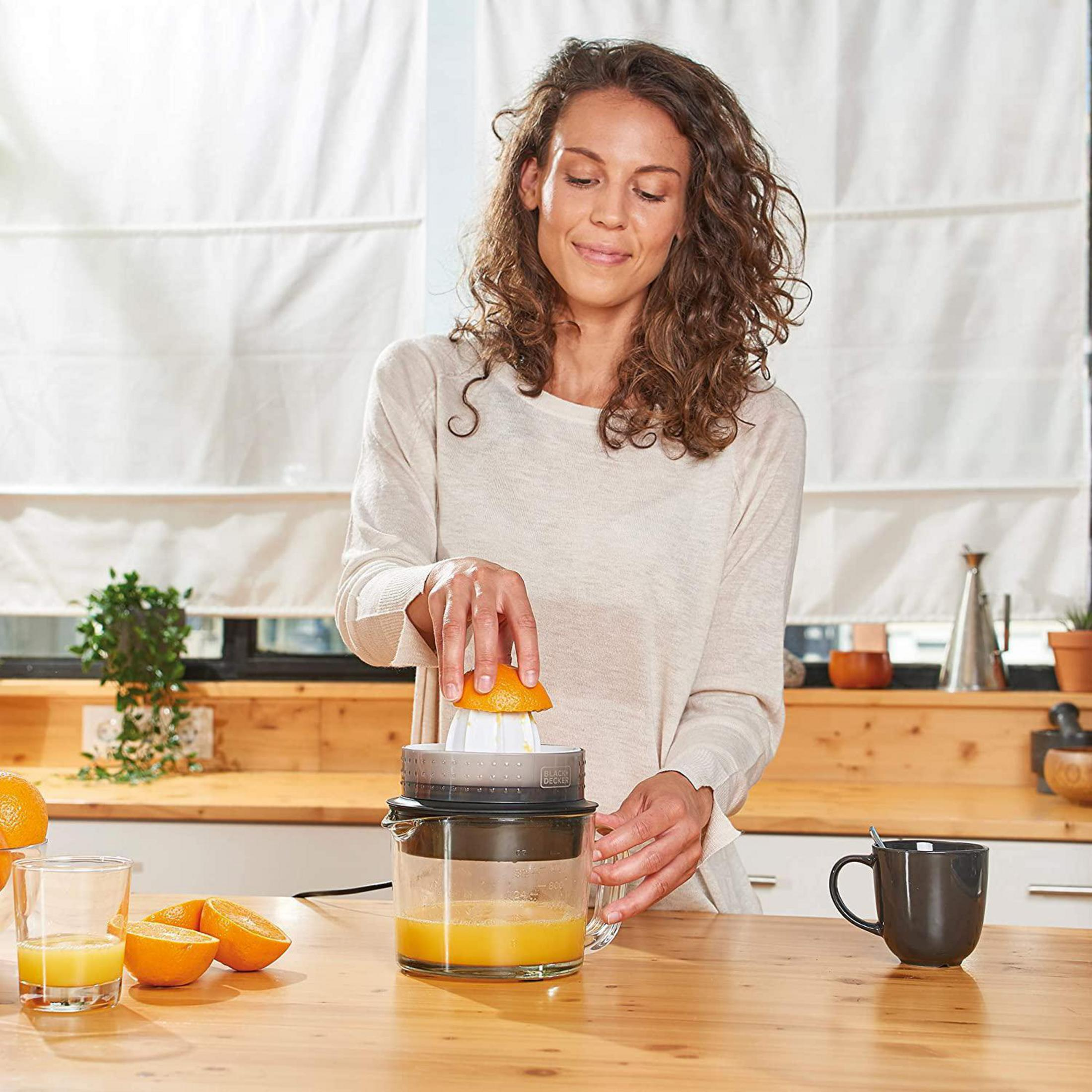 Mujer exprimiendo una naranja con un exprimidor. Ambiente de cocina. Encimera de madera.