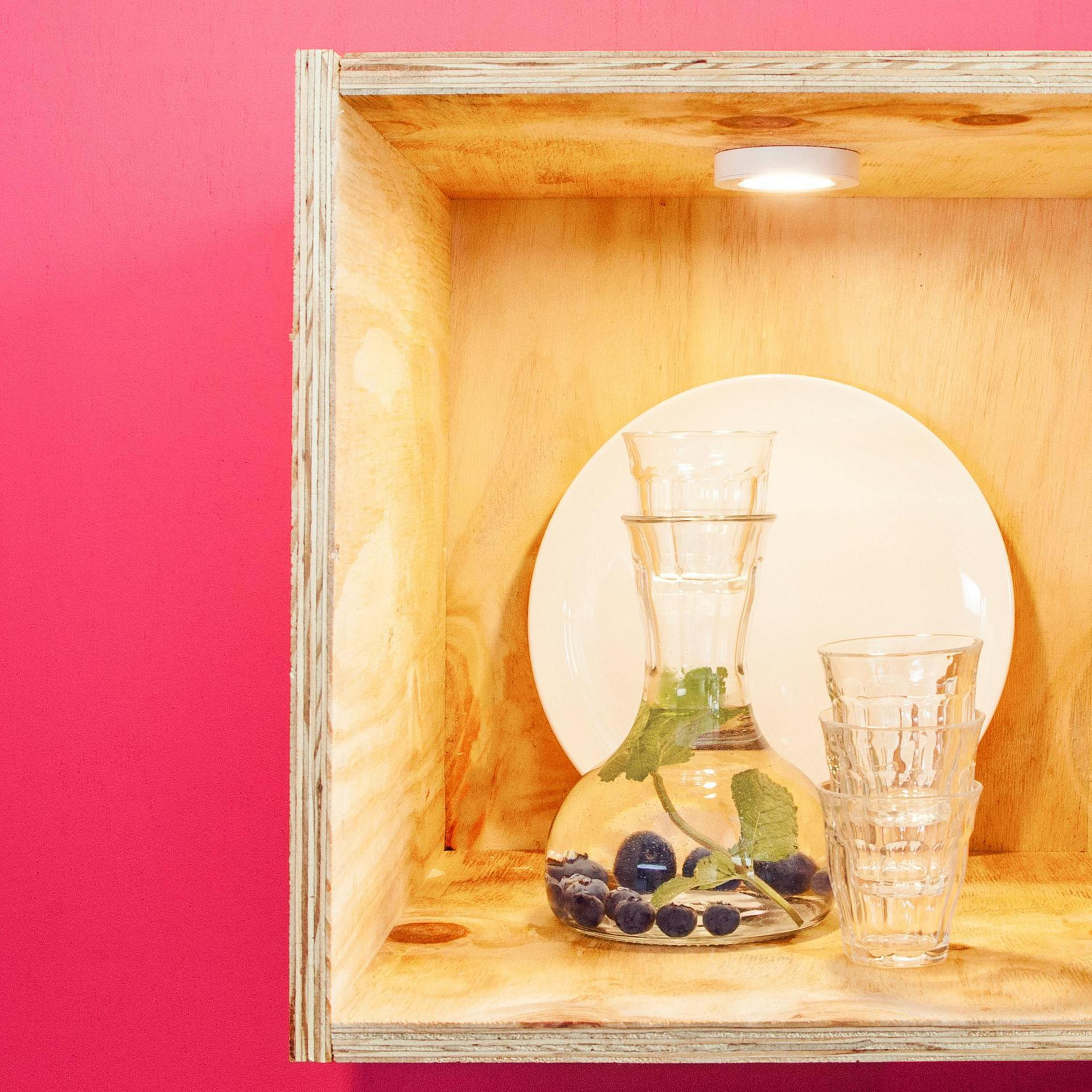 Drewniana półka z karafką, szklankami i talerzem. Różowe tło ściany.