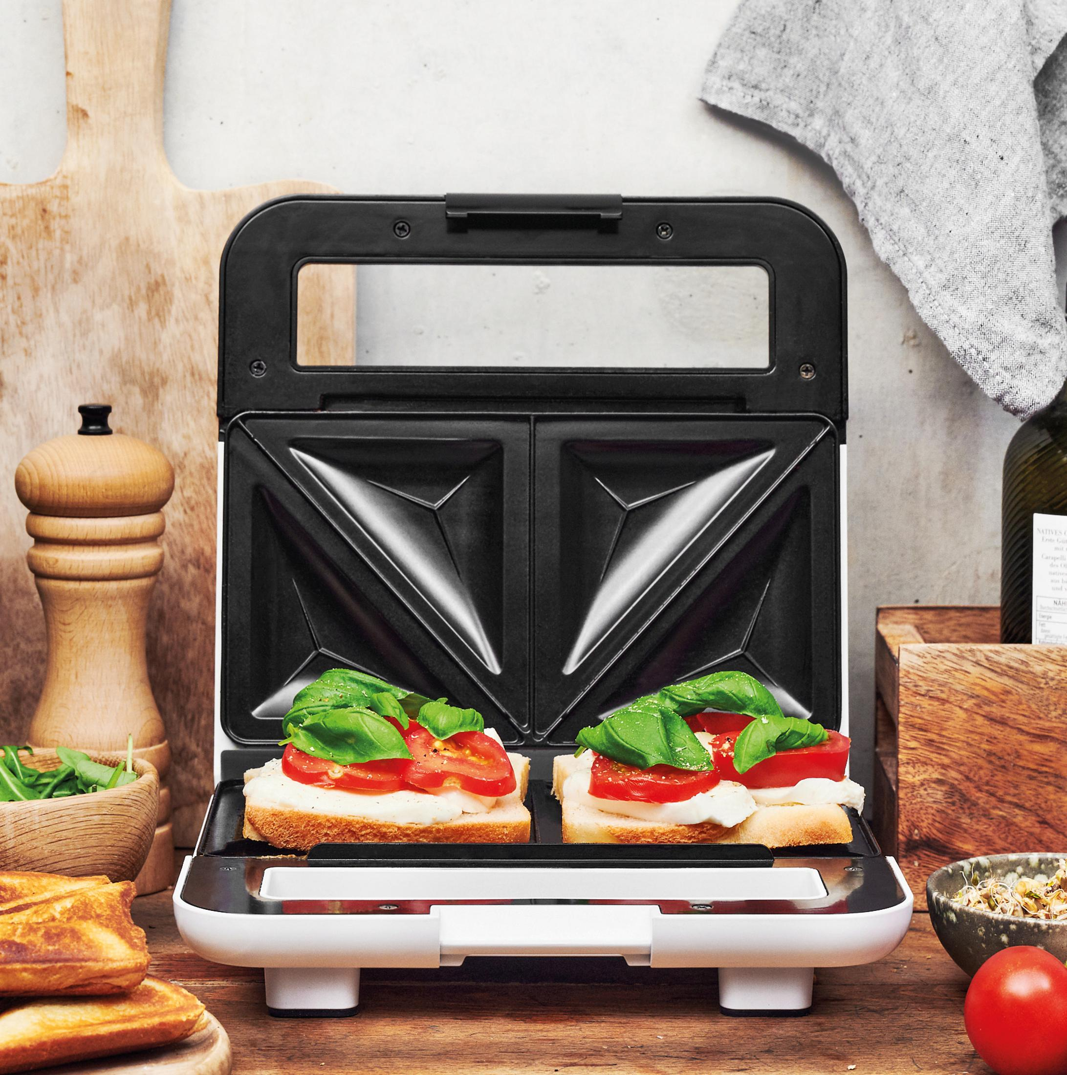 Sandwichmaker mit zwei Sandwiches. Tomaten und Basilikum sind auf dem Brot sichtbar.