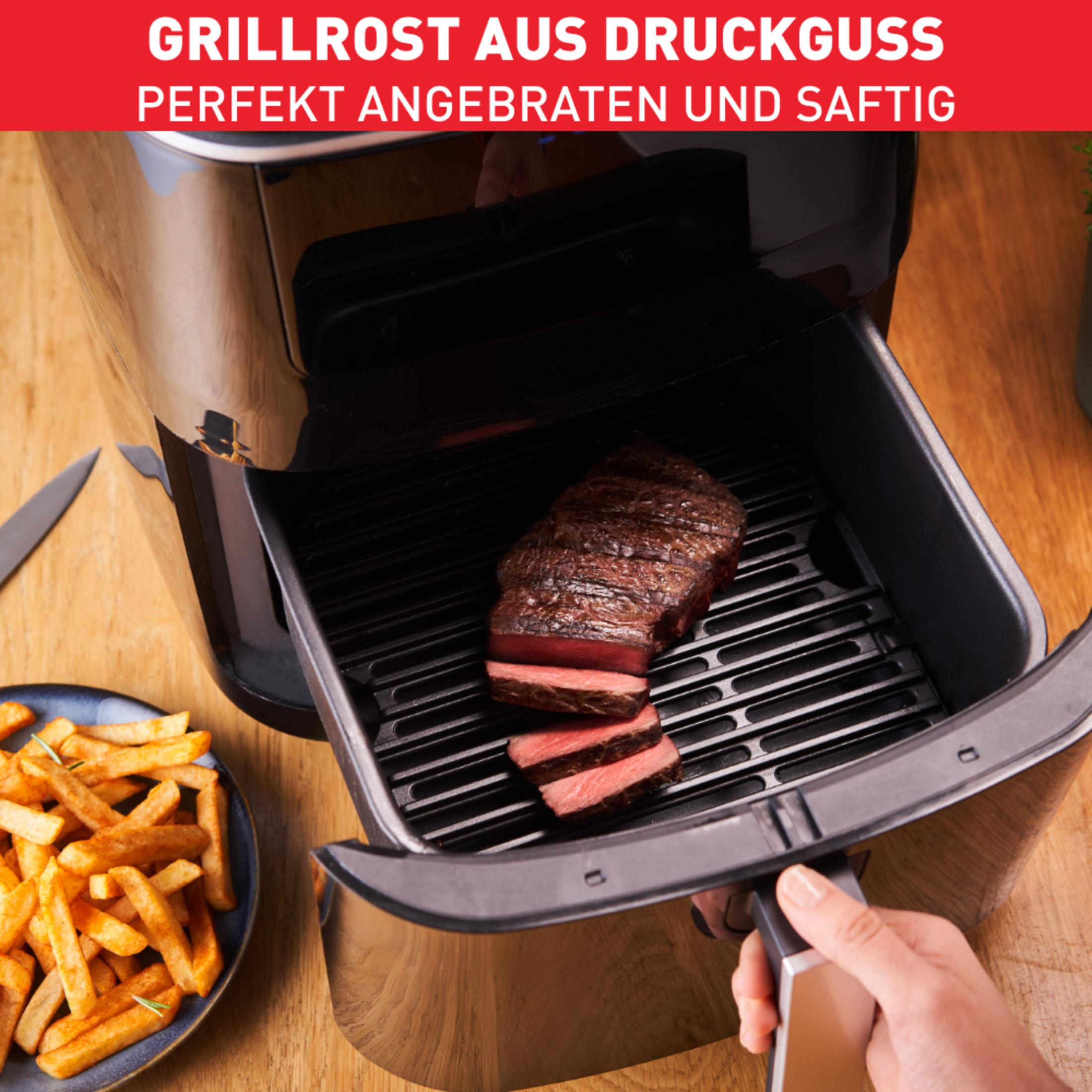 Stek i frytki w frytkownicy beztłuszczowej. Ręka sięga po uchwyt frytkownicy.