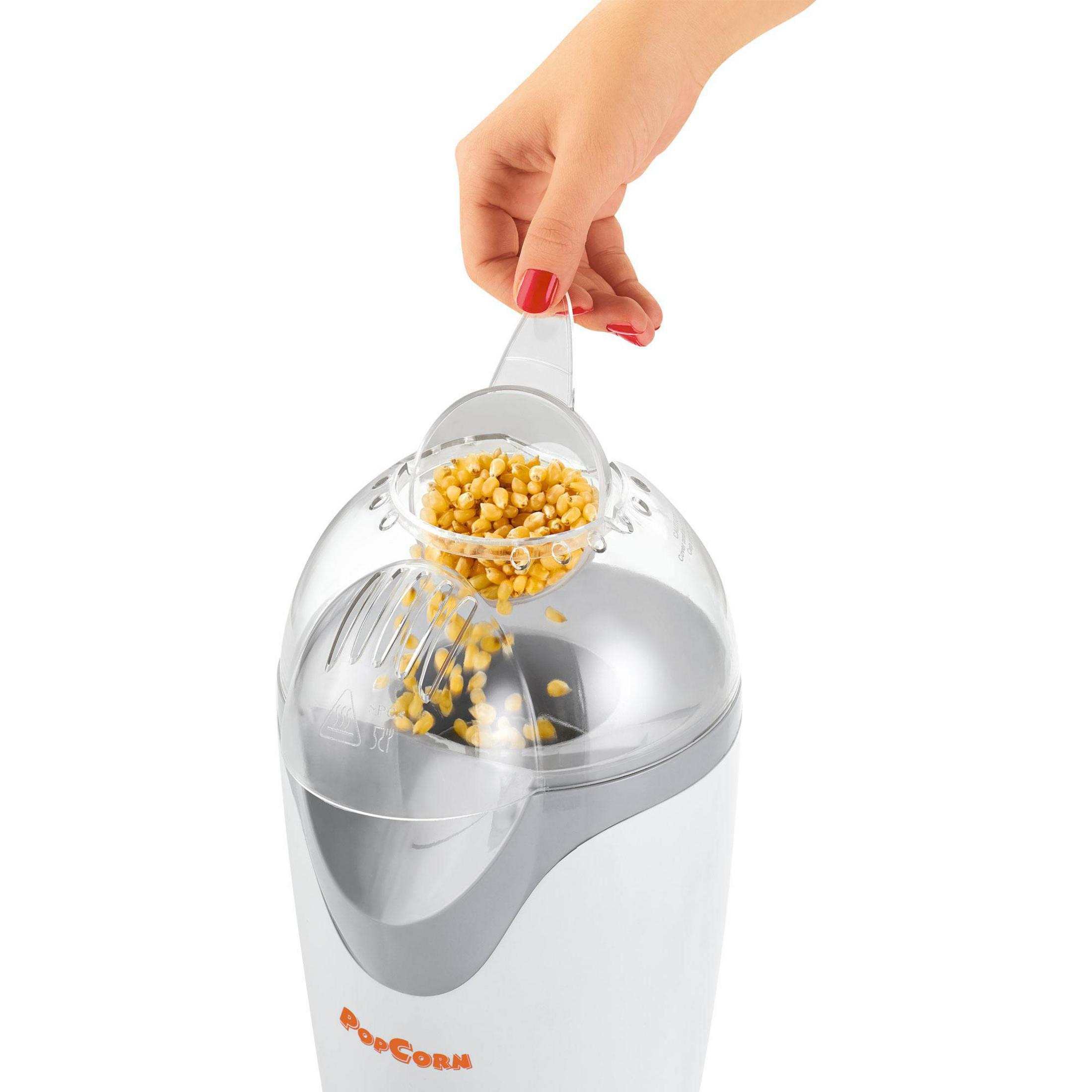 Die Hand einer Frau mit rotem Nagellack gießt Popcornkörner in eine weiß-graue Popcornmaschine.