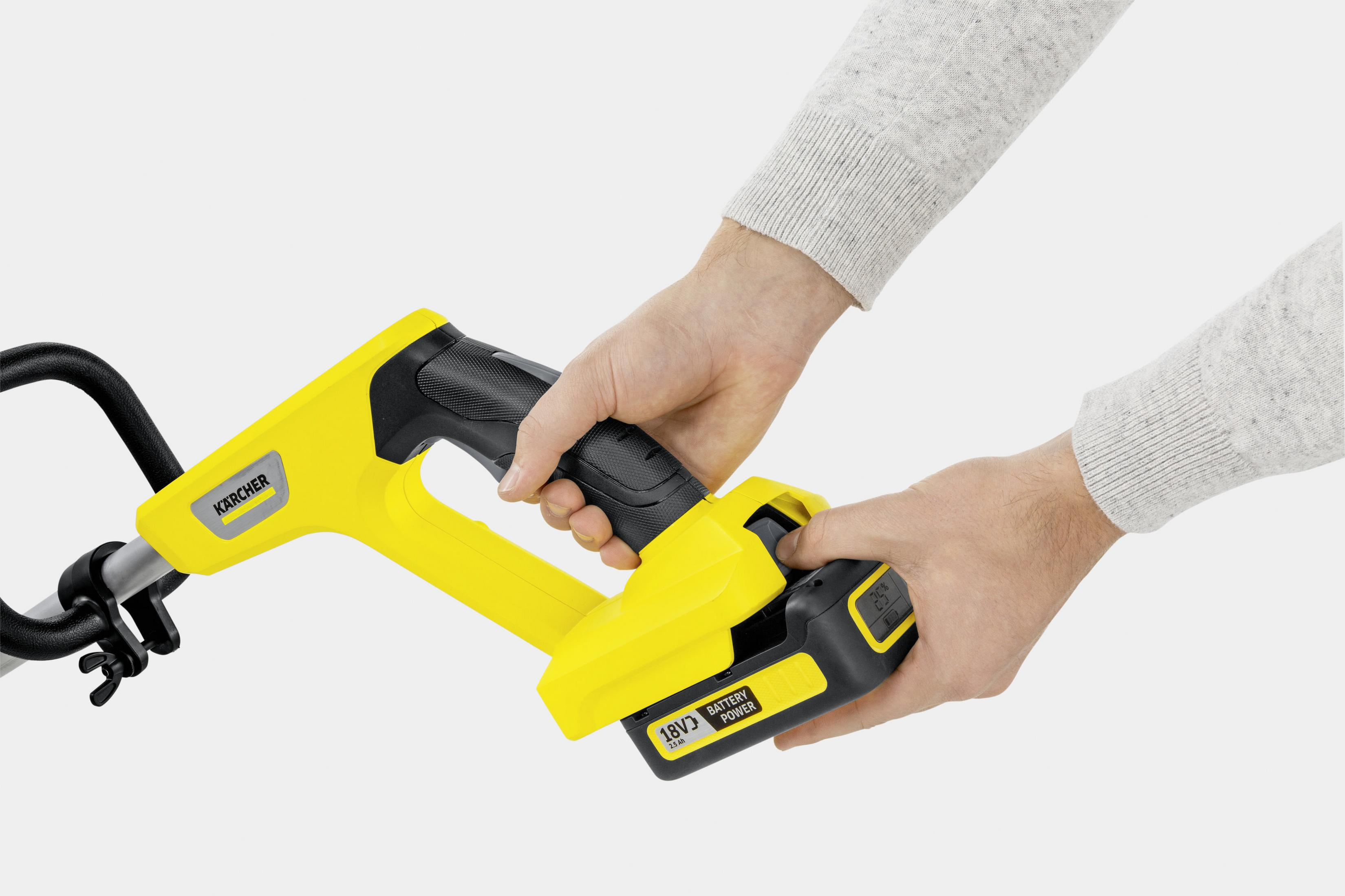 Osoba mocuje baterię do żółtej podkaszarki Karcher. Bateria jest czarno-żółta.