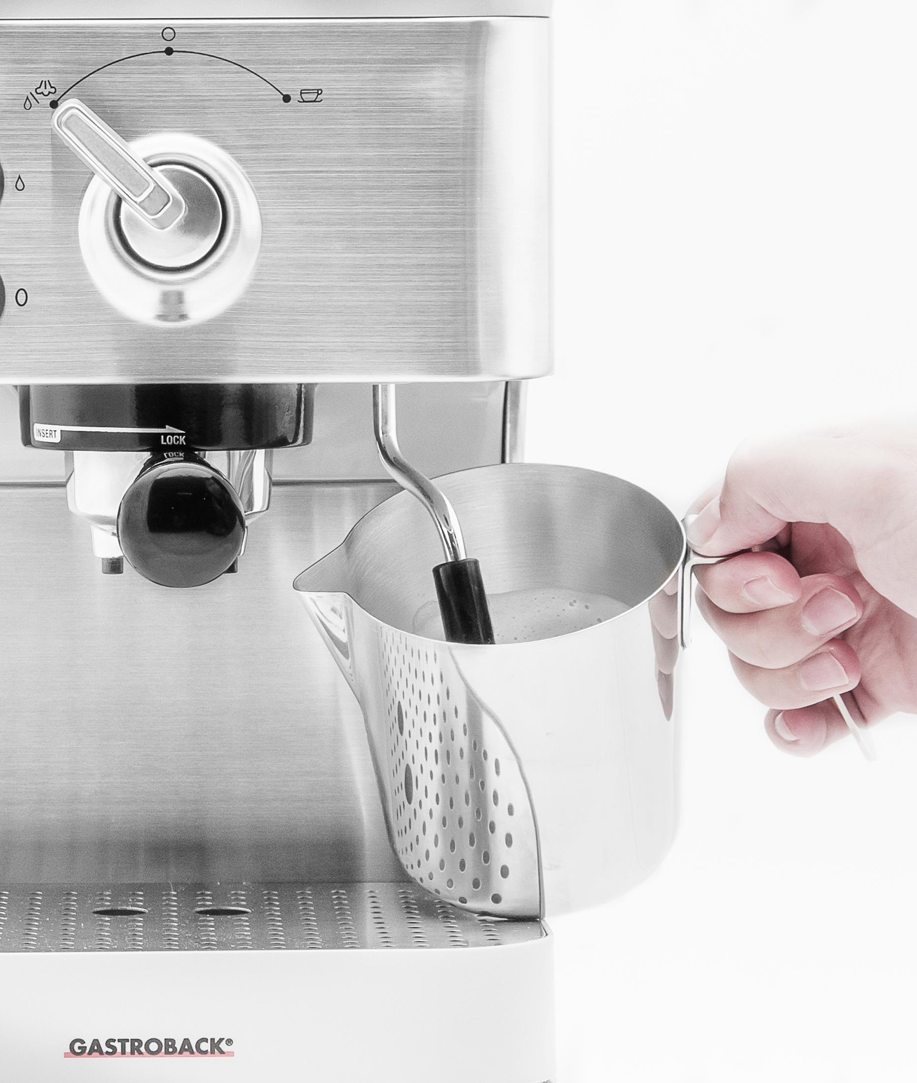 Espressomaschine aus Edelstahl mit silberner Kanne, die mit Milchschaum gefüllt wird, eine Hand hält die Kanne.