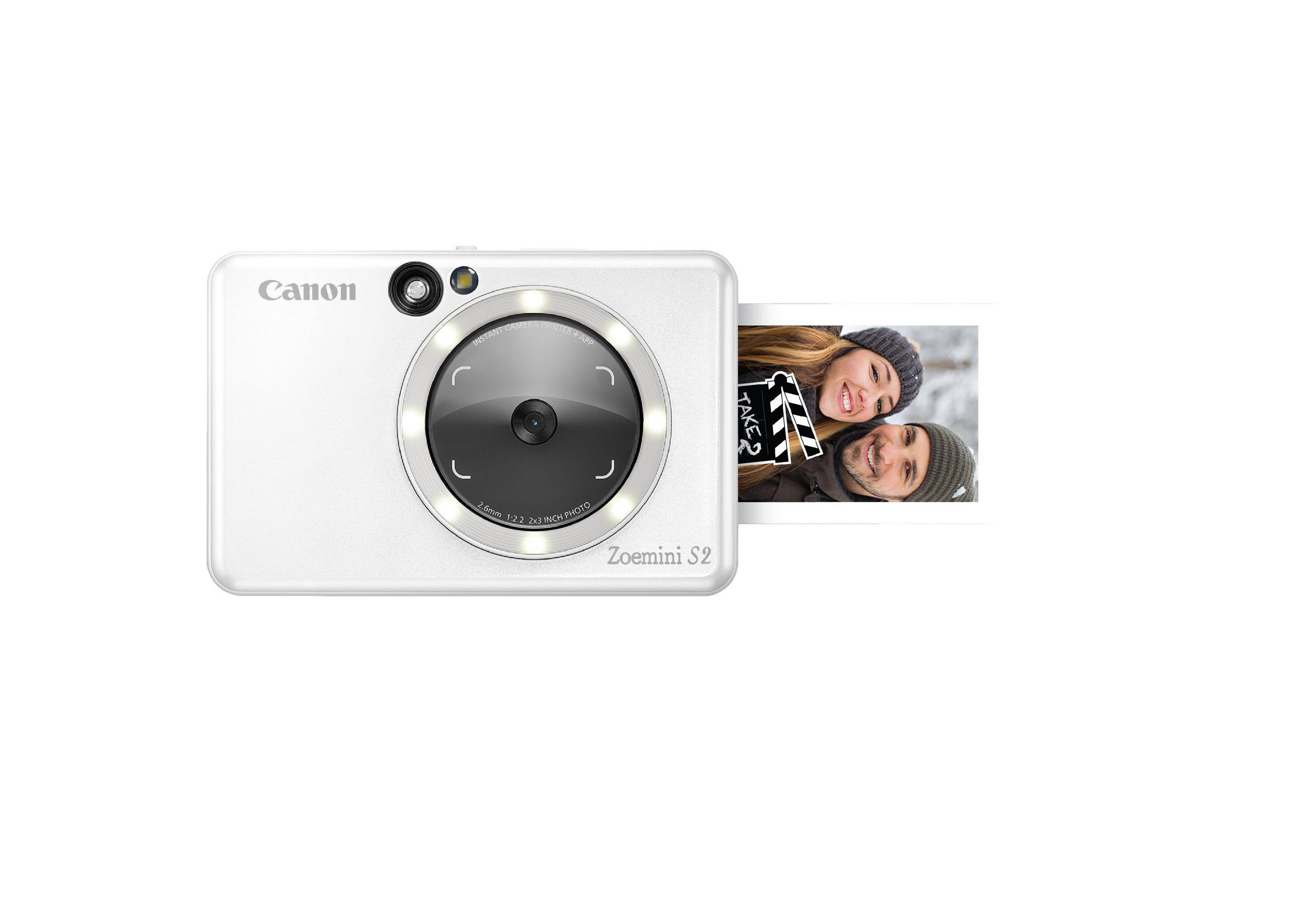 Biały aparat natychmiastowy Canon Zoemini S2 z wydrukiem zdjęcia. Czarny obiektyw, srebrne akcenty.
