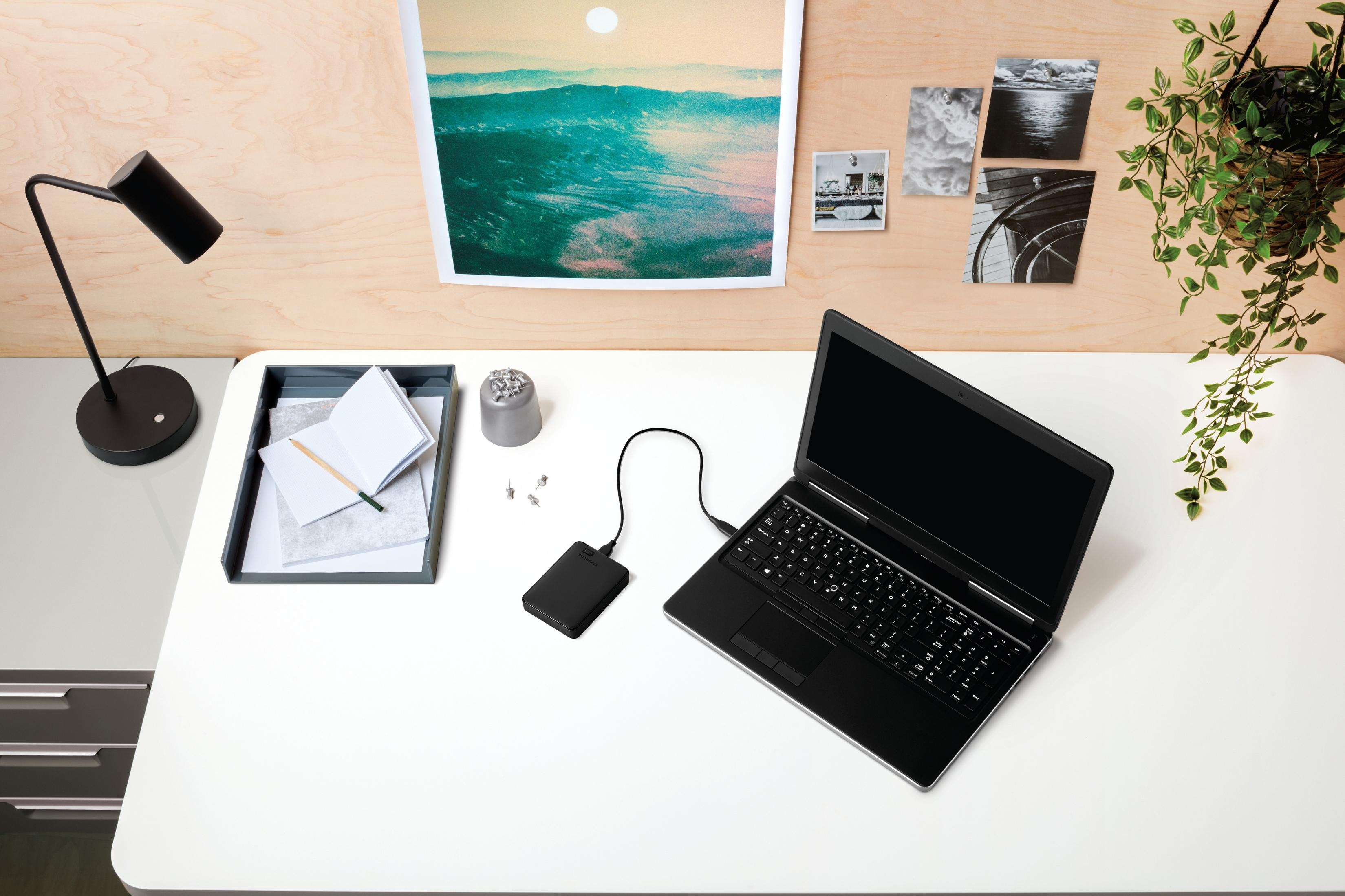 Ustawienia biurka: laptop, zewnętrzny dysk twardy, lampa, notatnik i zdjęcia.