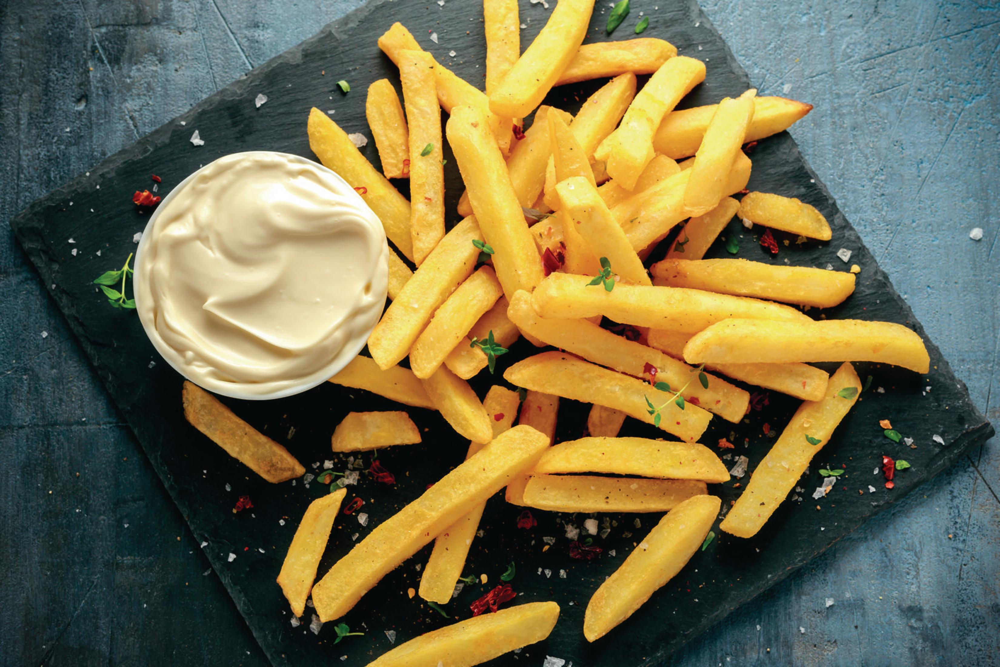 Frytki na czarnej tablicy z miską majonezu i niebiesko-szarym tłem.