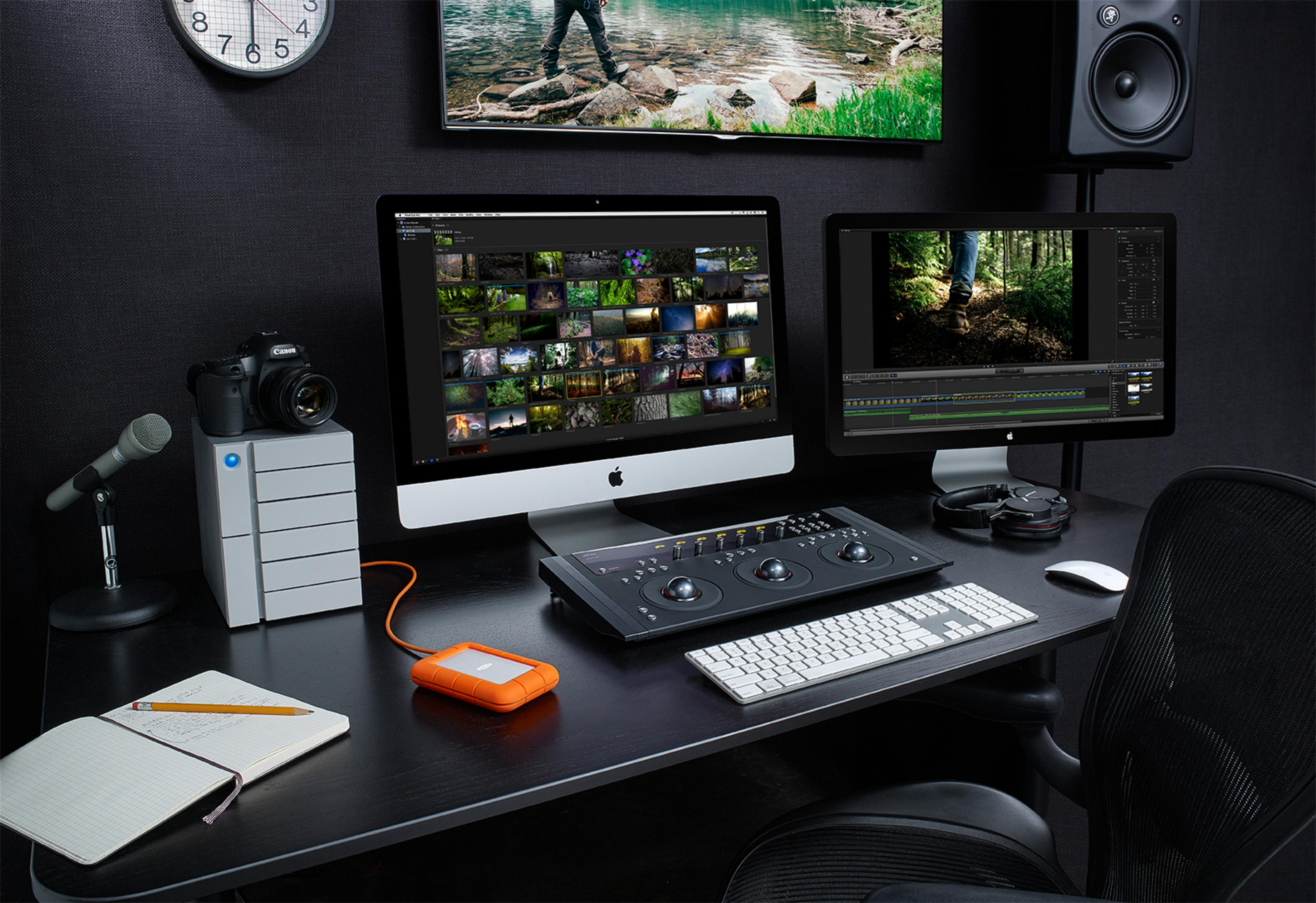 Biurko z dwoma monitorami, aparatem, narzędziami do edycji i notatnikiem. Czarne tło.