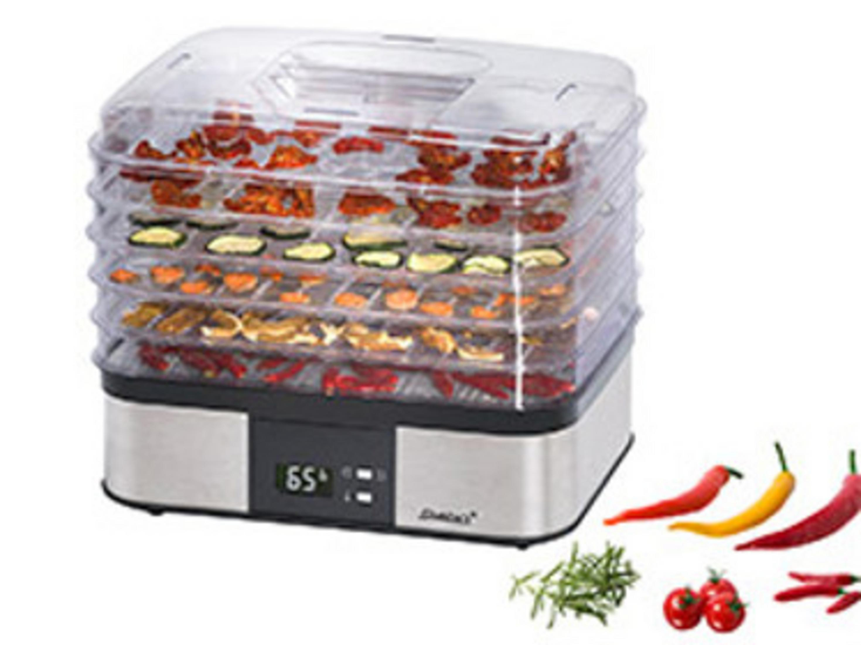 Ein Dörrgerät mit Tabletts mit getrocknetem Gemüse und Obst, in der Nähe Chilischoten.