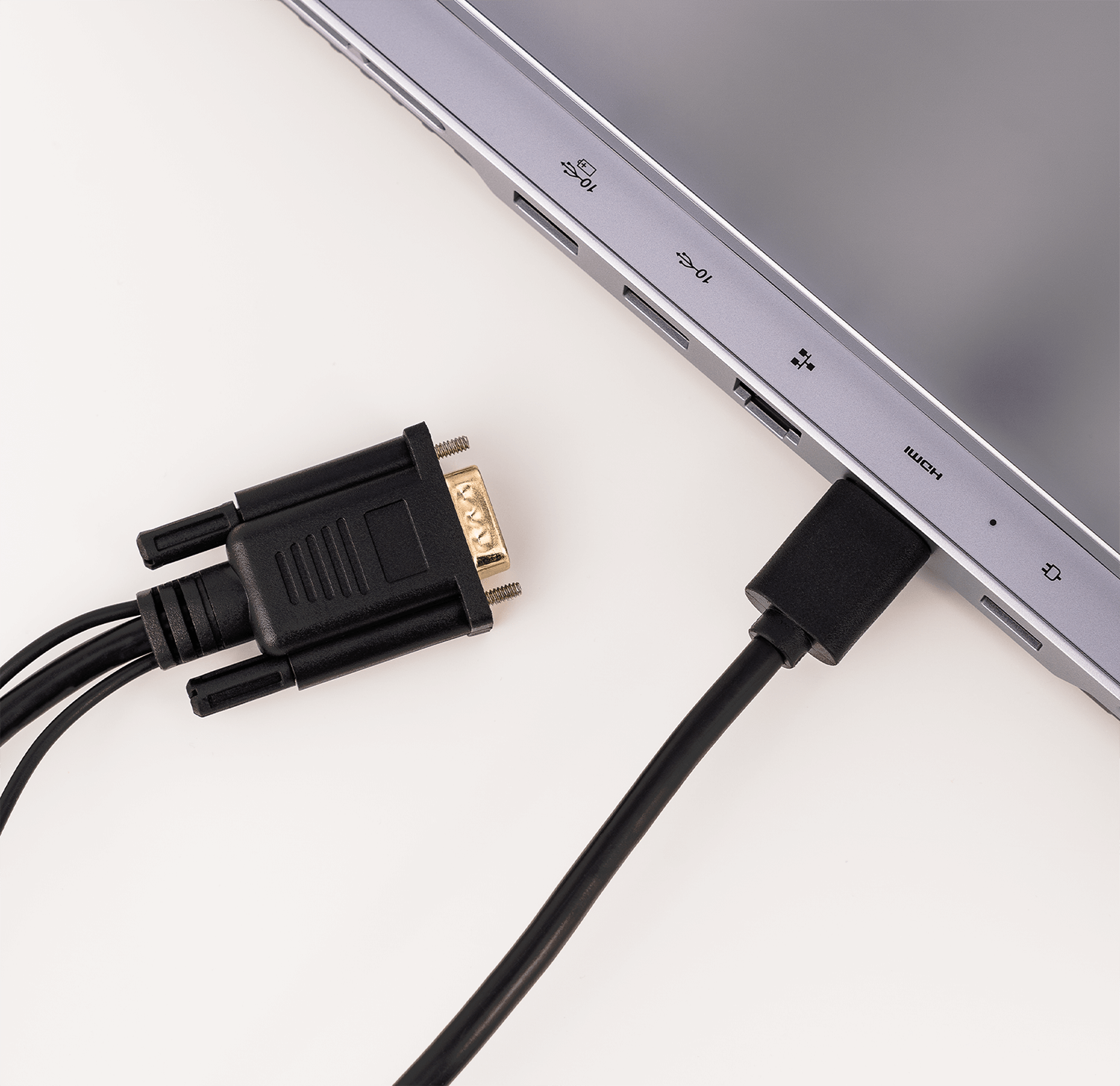 Laptop podłączony do czarnego kabla i złącza VGA, na białym tle. Laptop jest srebrny.