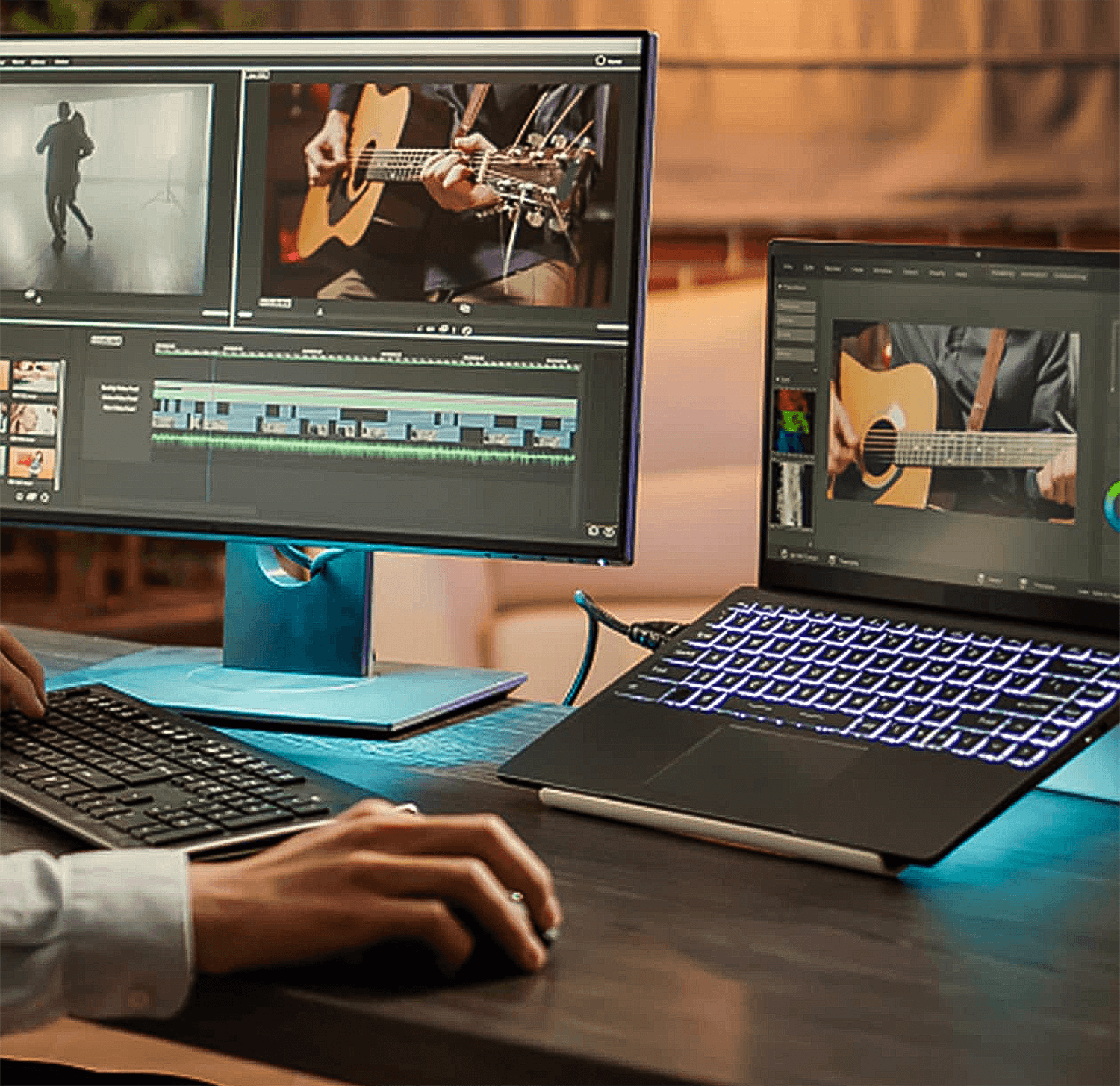 Osoba edytująca wideo na monitorze i laptopie. Klawiatura i mysz na pierwszym planie. Pokój jest słabo oświetlony.