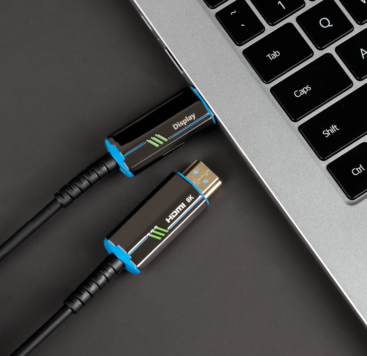 Czarny i niebieski kabel HDMI podłączony do laptopa, na ciemnej powierzchni.