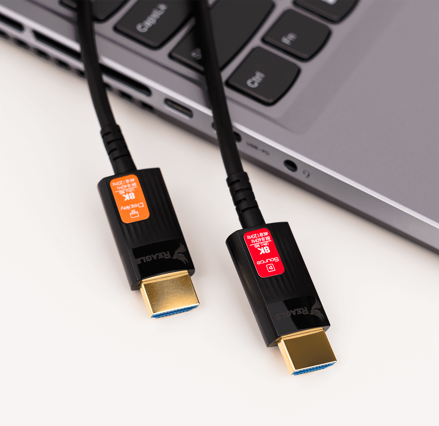 Dwa czarne kable HDMI ze złotymi złączami na srebrnej klawiaturze laptopa.