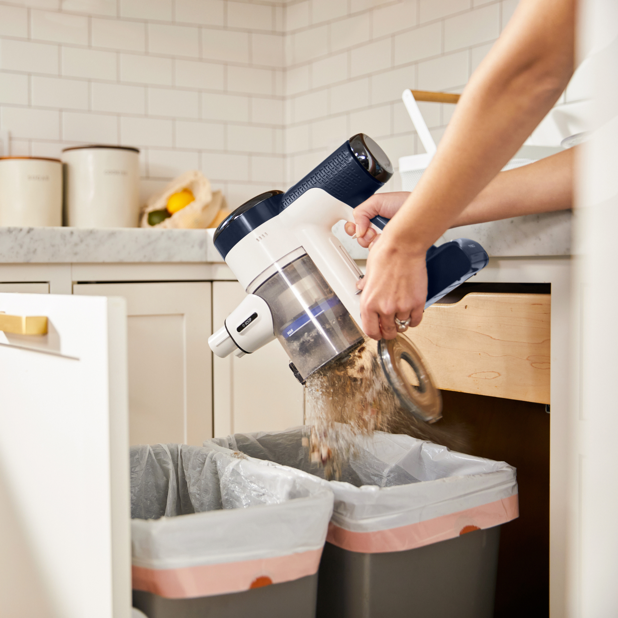 Una persona vaciando una aspiradora de mano en botes de basura en una cocina.
