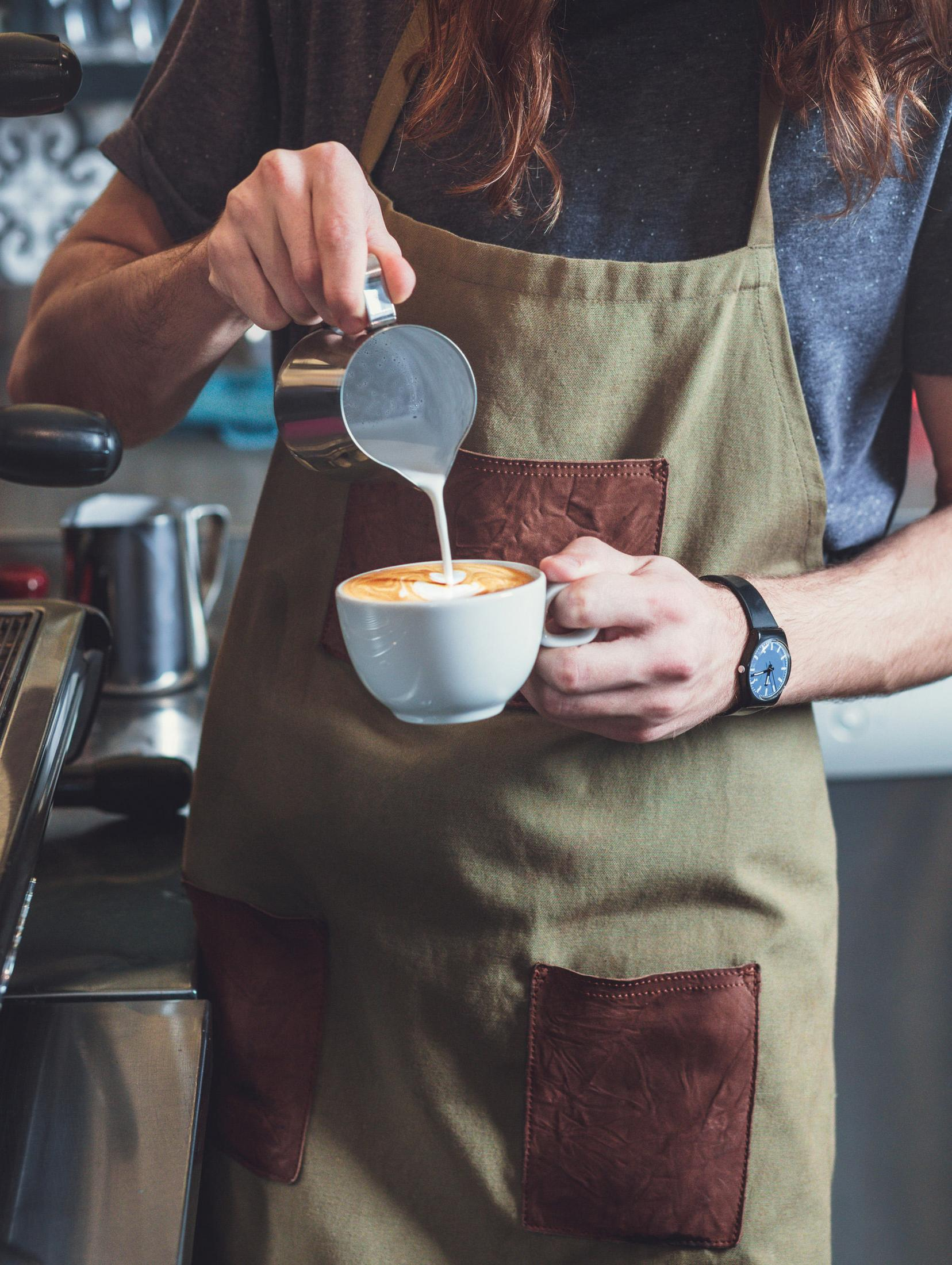 Barista nalewa mleko do filiżanki kawy, tworząc wzór.