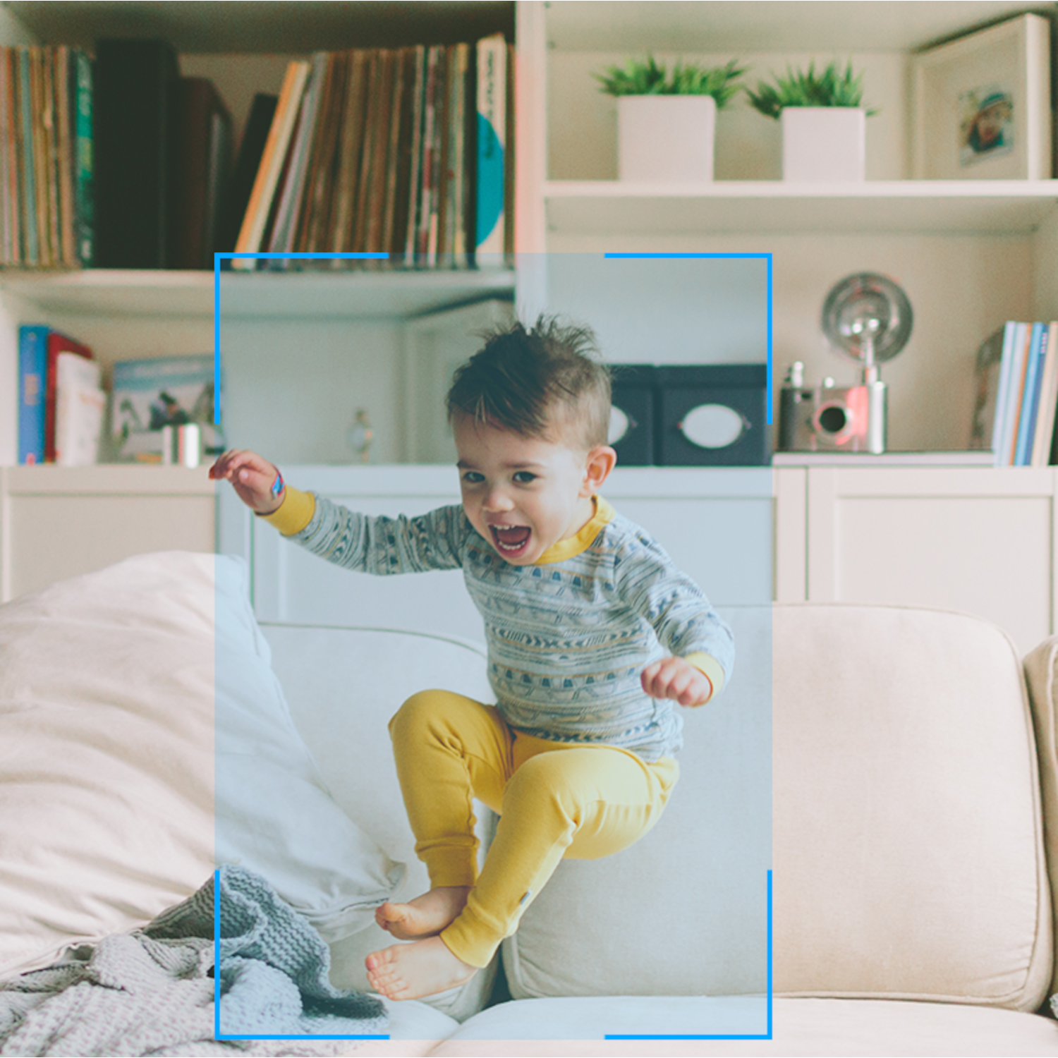 Dziecko skaczące na sofie w pomieszczeniu, z półką na książki w tle.