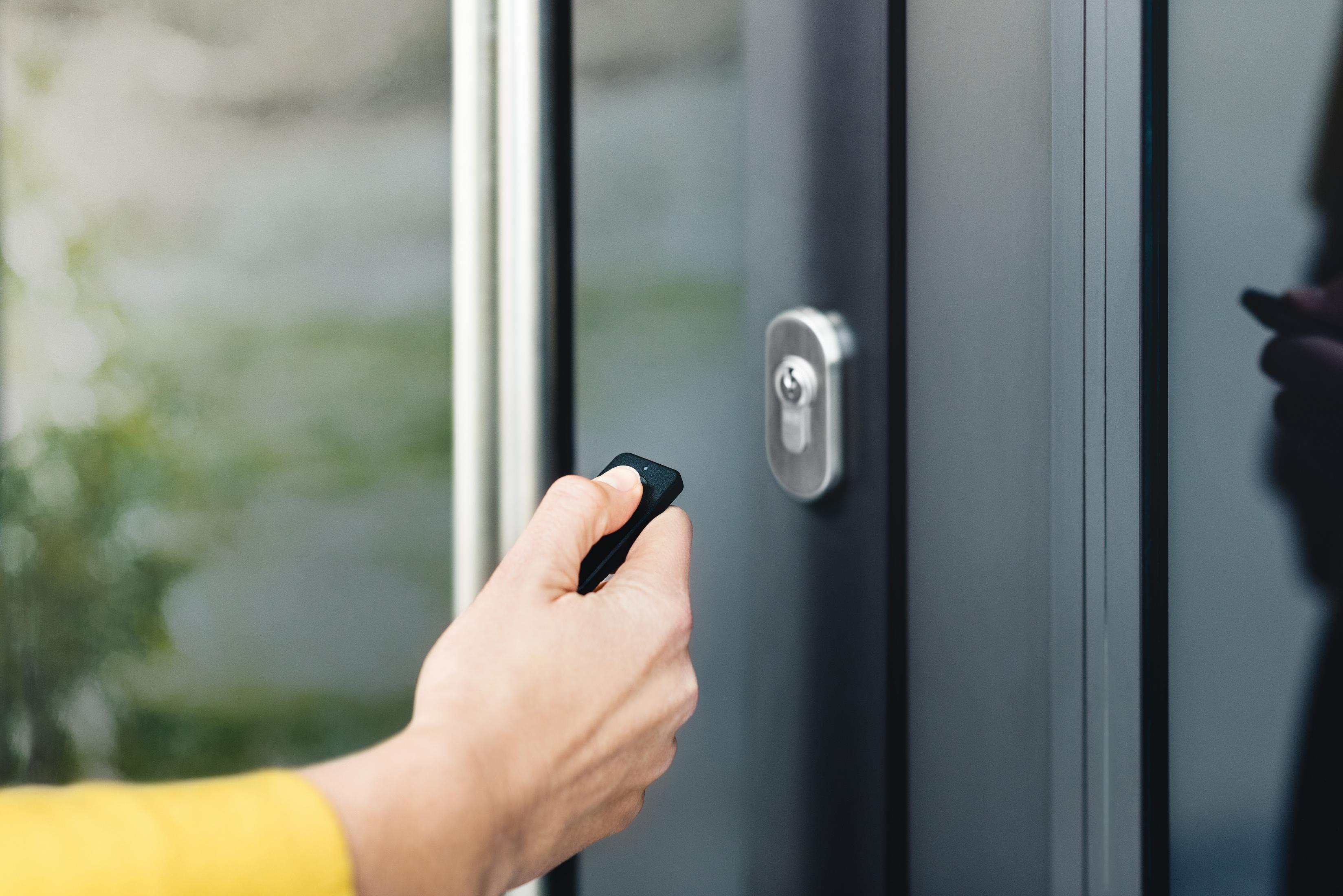 Hand holding a remote to unlock a door. Door has a silver handle and lock.