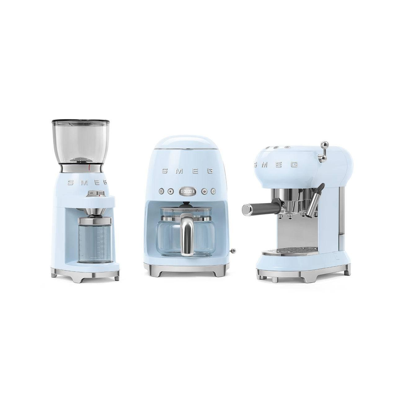 Tre elettrodomestici SMEG azzurri: un macinacaffè, una macchina per caffè filtro e una macchina per espresso.