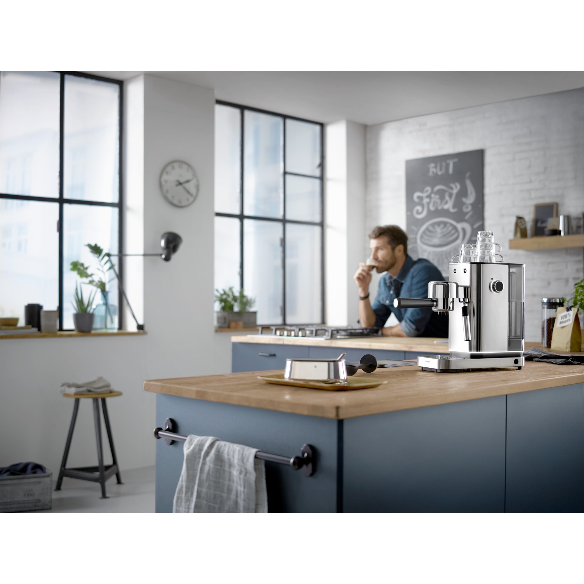 Keuken met een man die koffie drinkt. Espressomachine op het aanrecht. Achtergrond met klok en ramen.