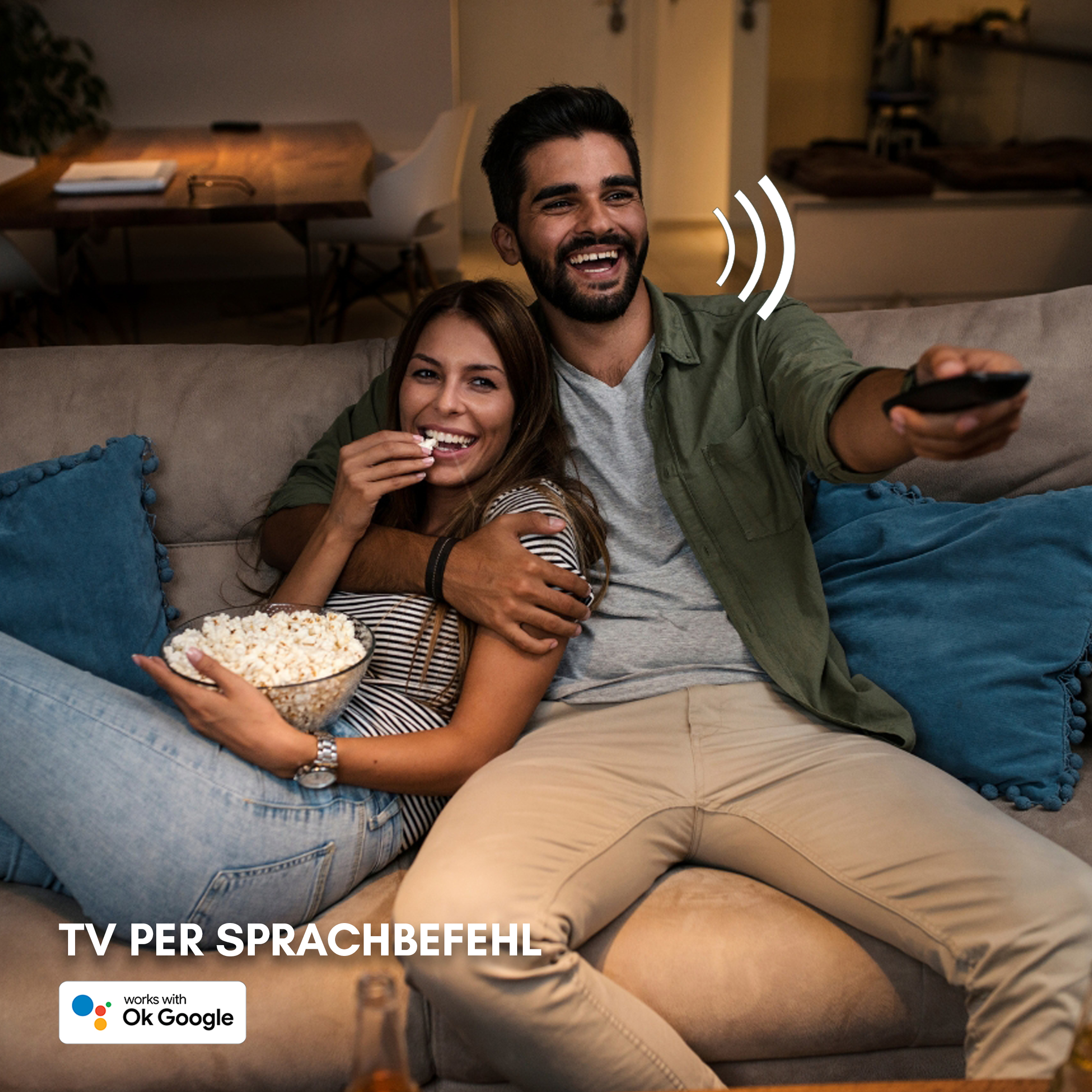 Ein Paar auf dem Sofa beim Fernsehen, der Mann hält eine Fernbedienung, die Frau isst Popcorn.