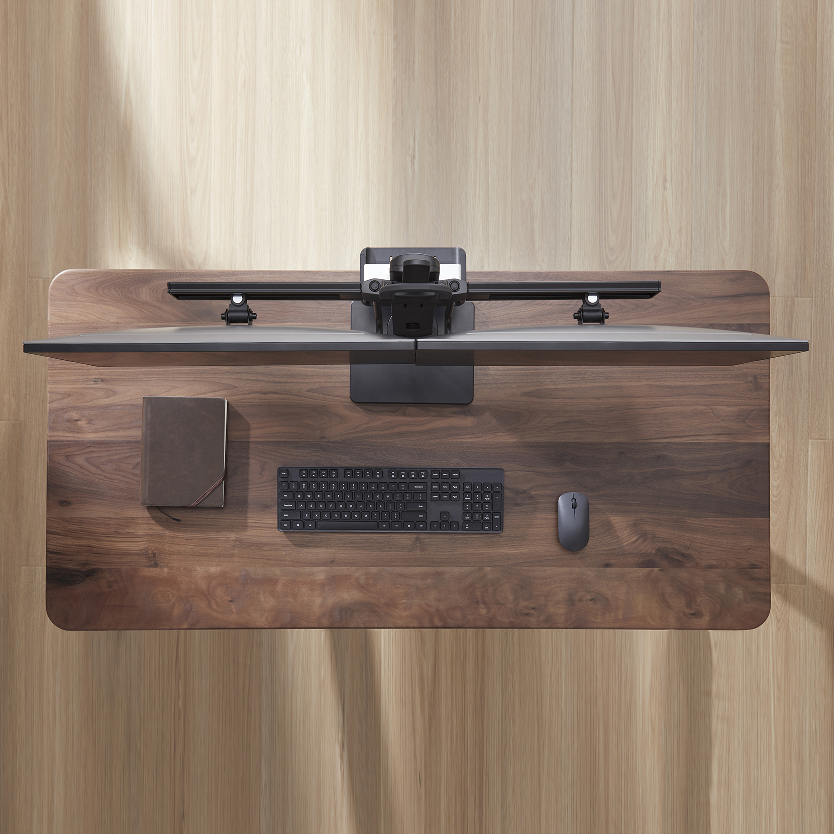 Draufsicht auf einen Holzschreibtisch mit Monitor, Tastatur, Maus und Notizbuch.
