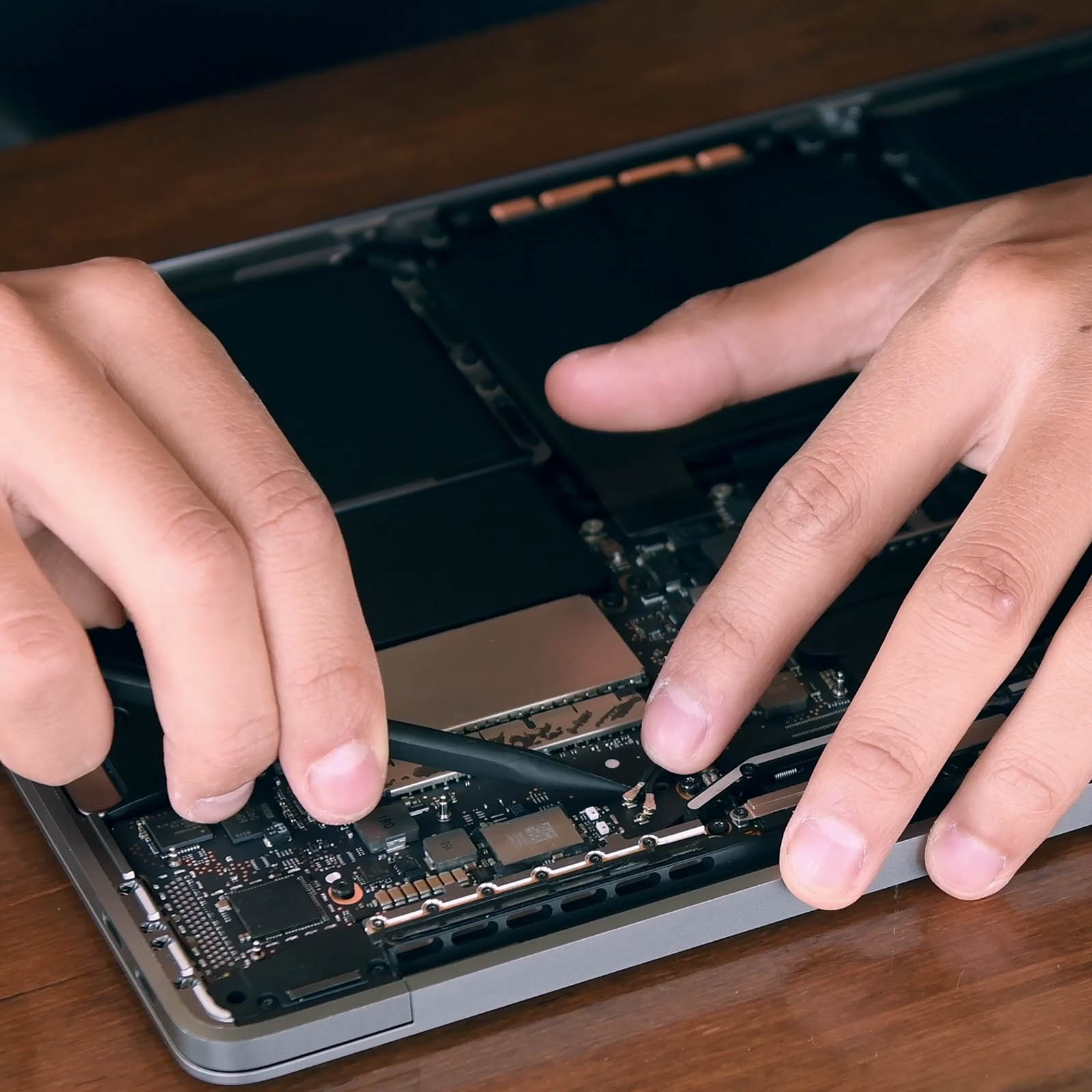 Hände zerlegen mit einem Werkzeug einen Laptop. Die internen Komponenten des Laptops sind sichtbar.