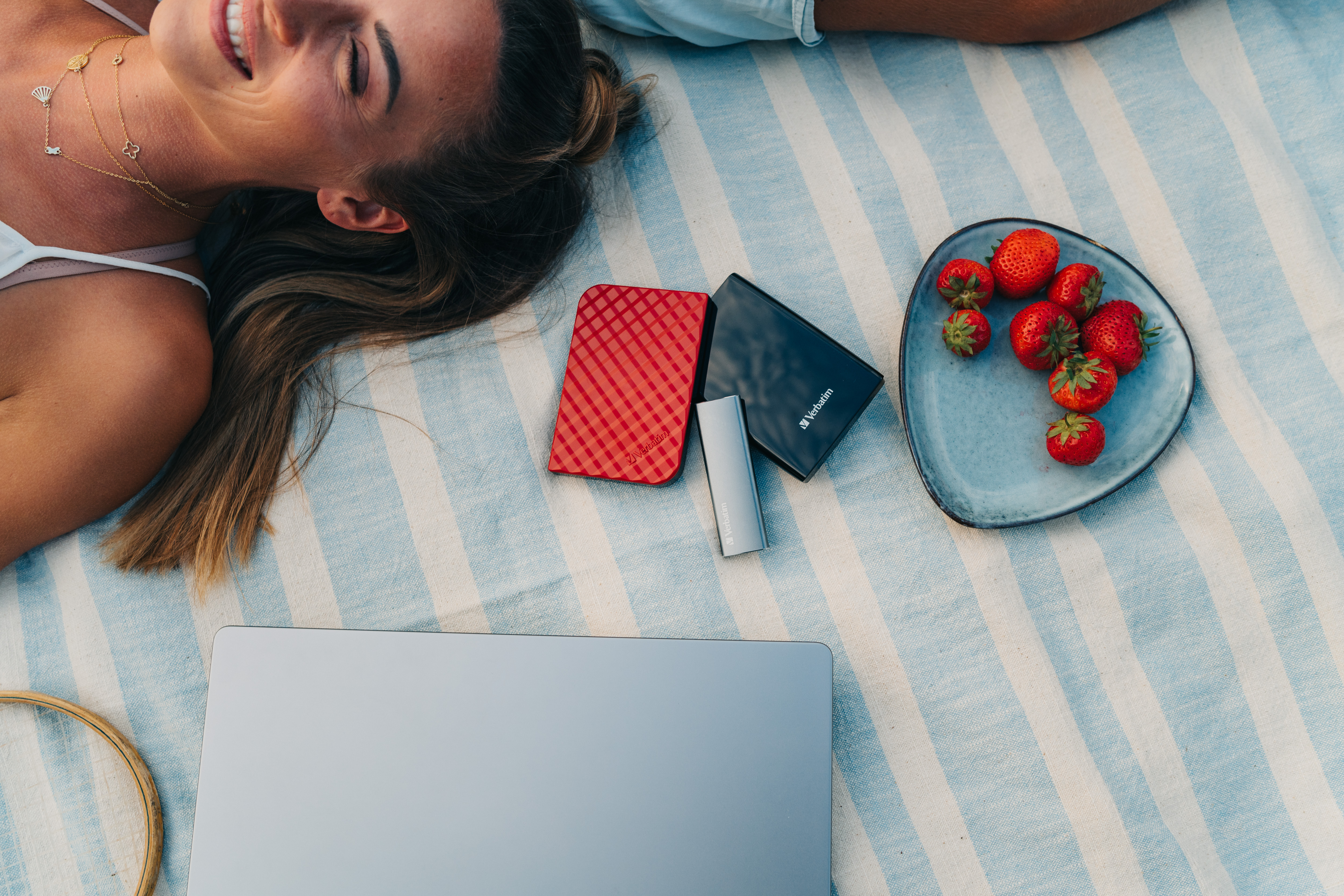 Frau auf Picknickdecke mit Erdbeeren, Laptop und zwei externen Festplatten.