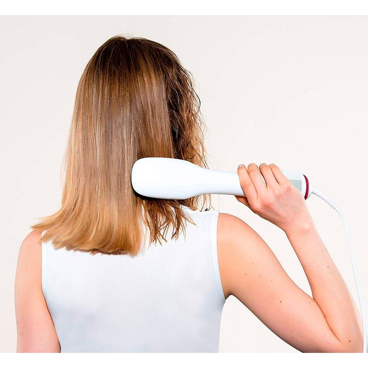 Una mujer usando un secador de pelo blanco para secar su cabello.