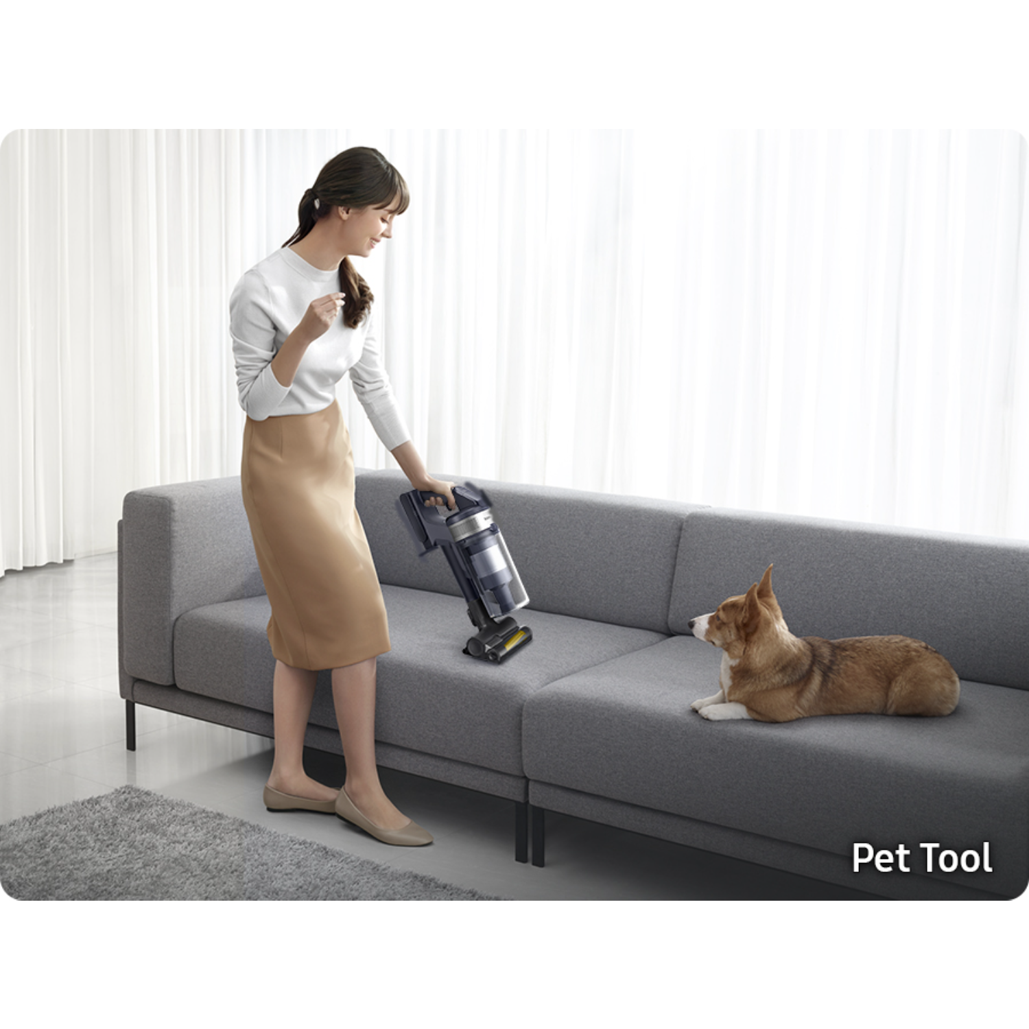 Kobieta odkurza szarą kanapę, pies patrzy. Widoczna etykieta 'Pet Tool'.