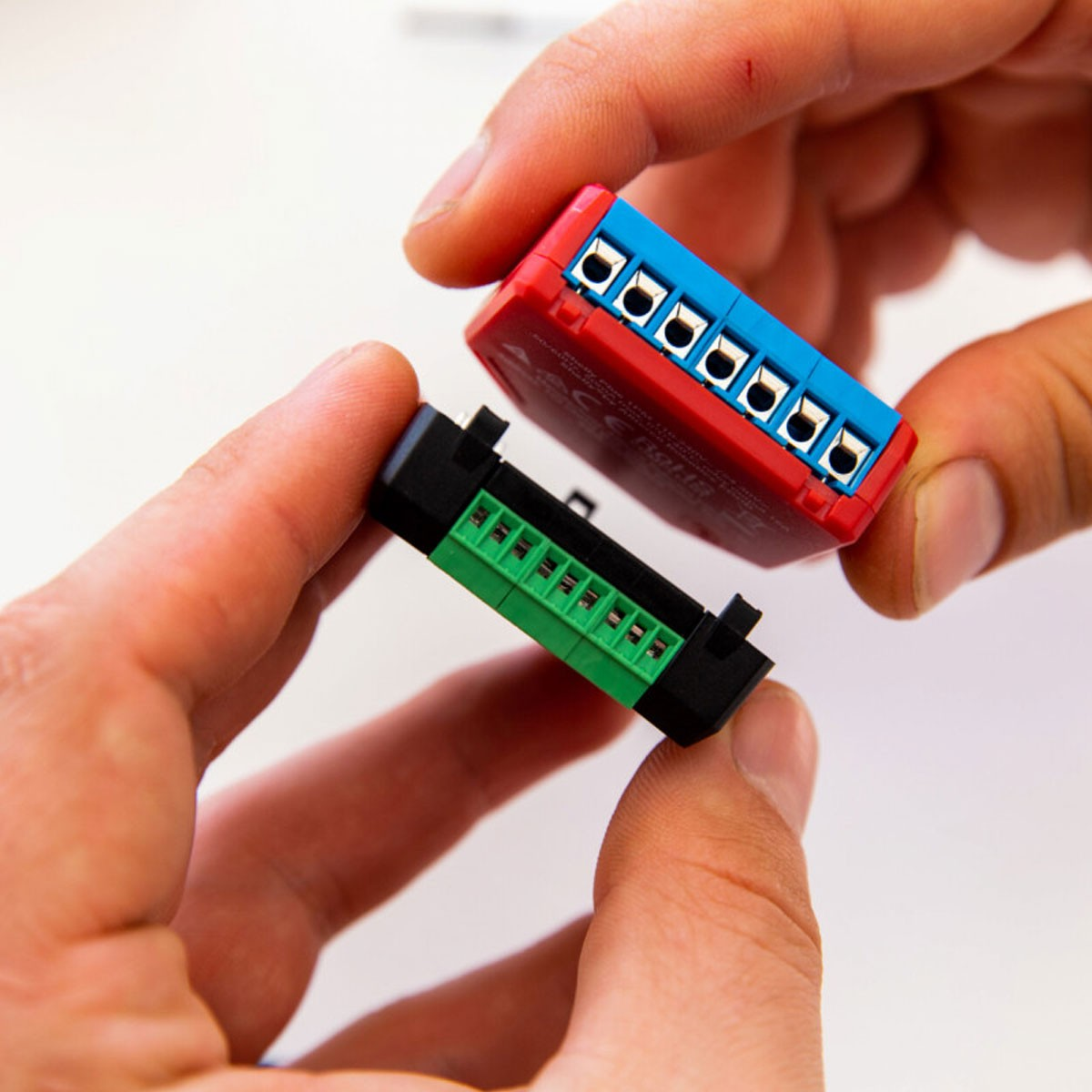 Manos sosteniendo dos módulos electrónicos, uno rojo y otro verde con conectores.