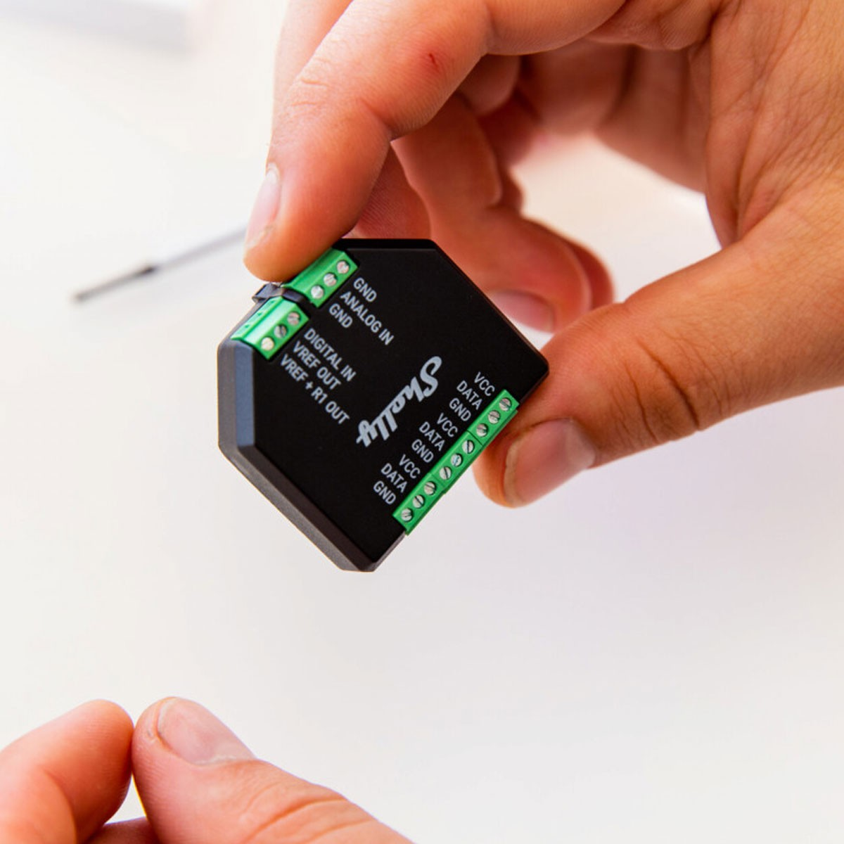Manos de una persona sosteniendo un componente electrónico negro con terminales verdes, etiquetado.