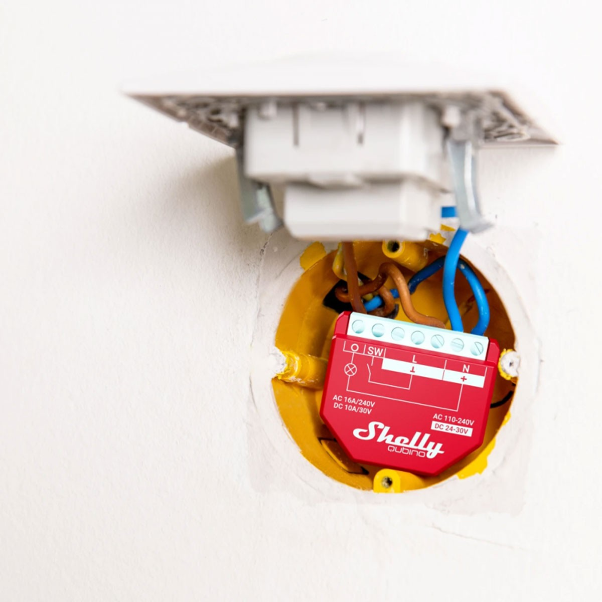 Rotes Smart-Home-Gerät in einer Wand, mit freiliegenden Drähten und einer weißen Steckdose.